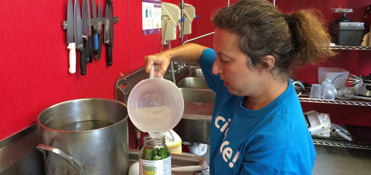 Robin Doroshow adds brine to a jar of cucumbers. The cukes will ferment into pickles.