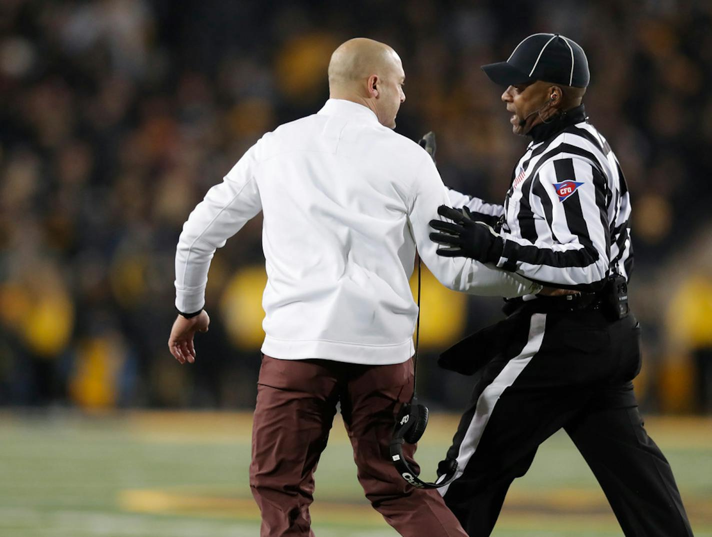 Minnesota head coach P.J. Fleck, left, is escorted back to the sideline by an official after running onto the field.