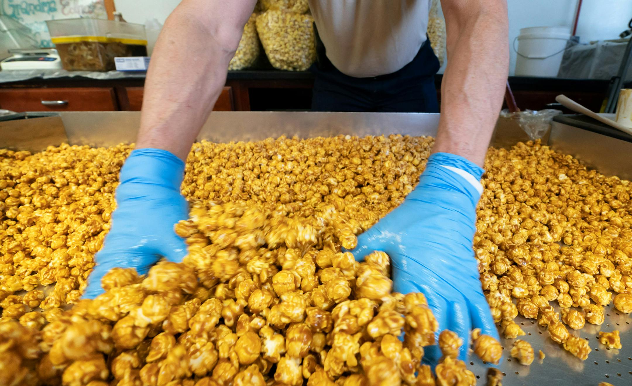 Dave Blomquist ran his gloved fingers through a hot fresh batch of Grandma Edna's Caramel Corn on the cooling table. ] GLEN STUBBE • glen.stubbe@startribune.com Tuesday, April 17, 2018 Dave and Cindy Blomquist make popcorn, label packages and whatever else it is they do as a two-person operation. Grandma Edna's is a small, boutique popcorn brand sold in grocery stores throughout the Twin Cities and is one of several popcorn brands capitalizing on the growing popularity of ready-to-eat (pr