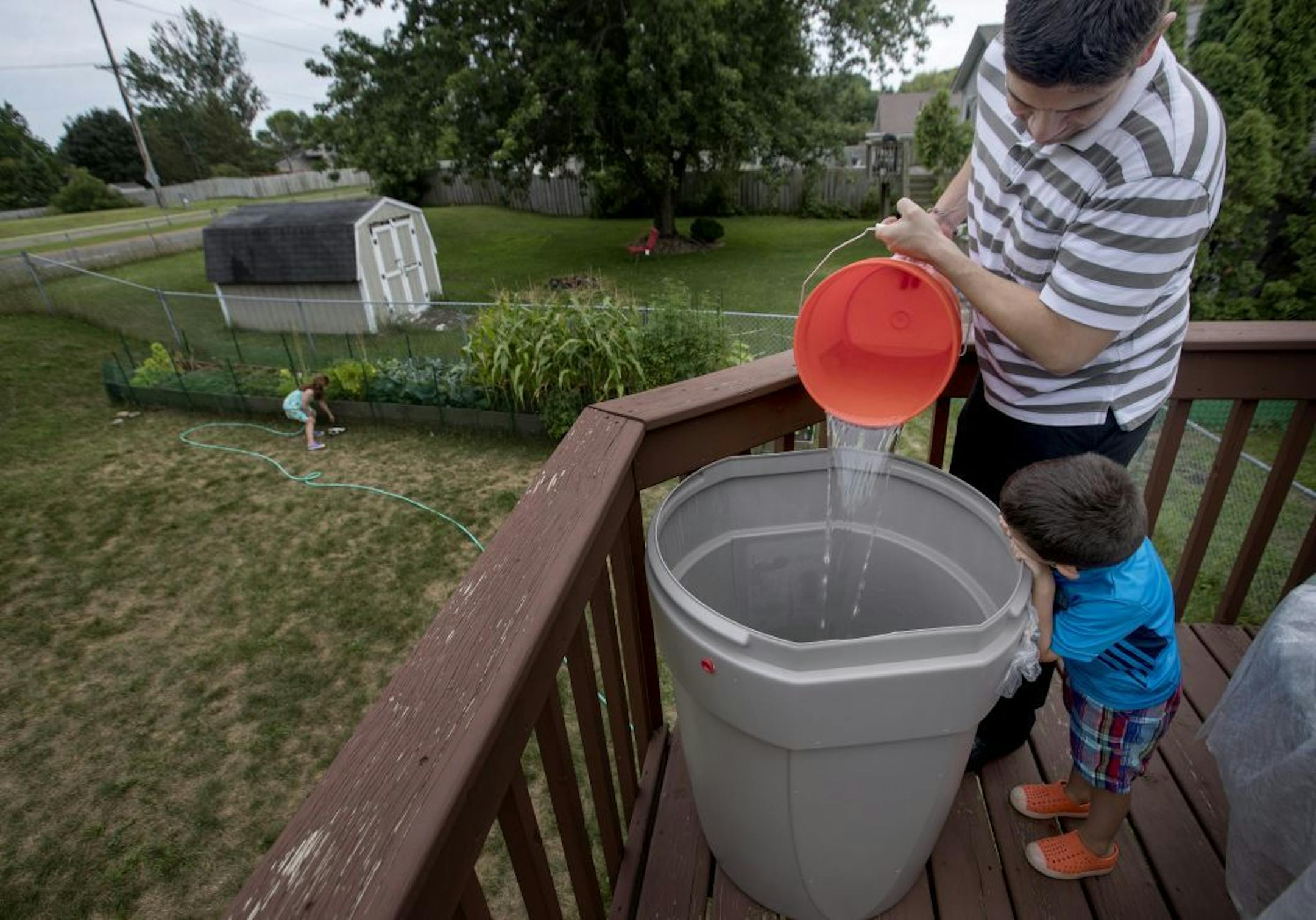 Teddy Cuellar, 4, watched his father Matt pour water from the shower into a rain barrel on the deck of their Cottage Grove home. The family waters their garden from the barrel.