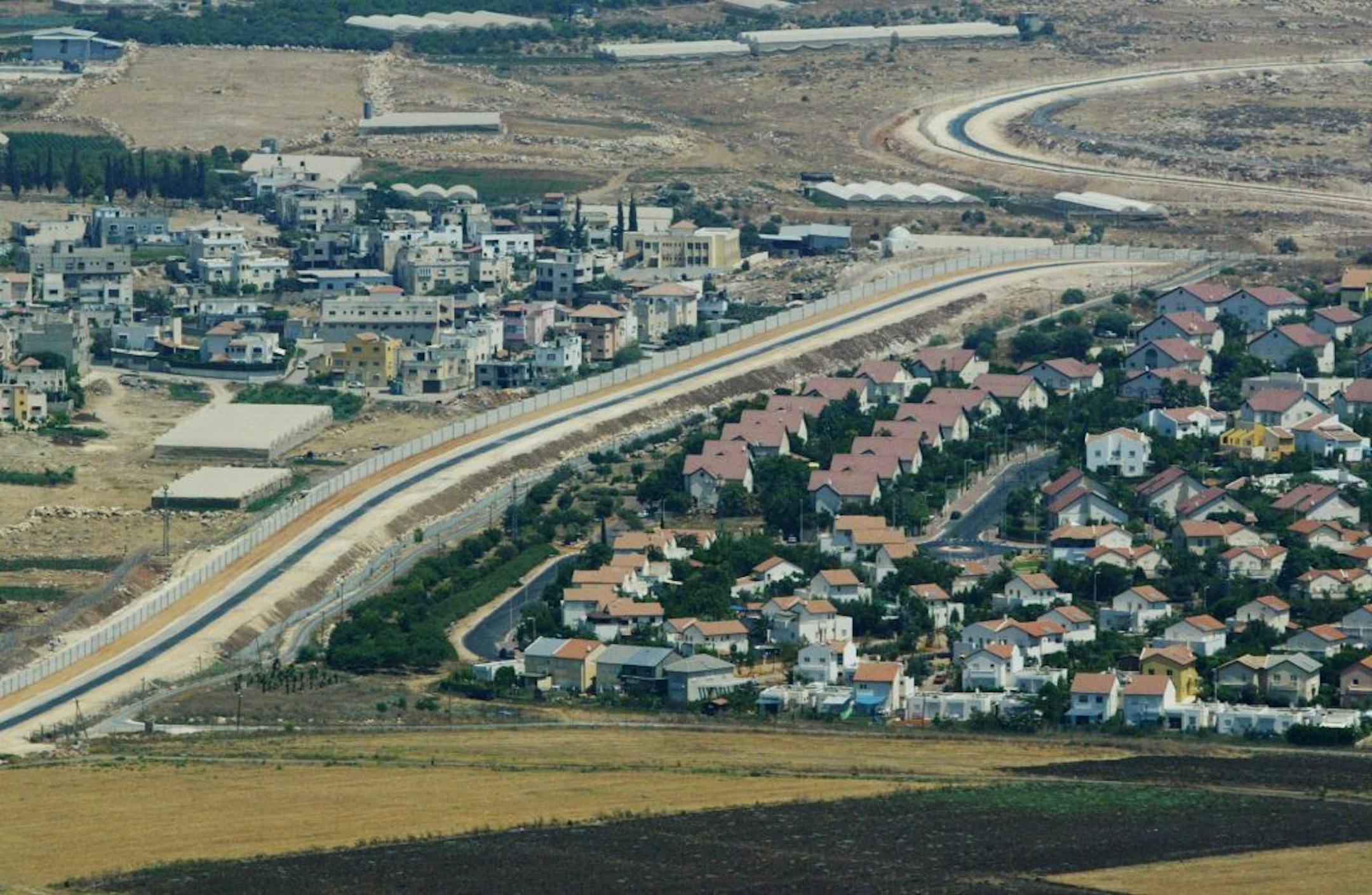 FILE - This Tuesday, July 29, 2003 file photo is an aerial view over West Bank showing a Palestinian village, left, and a Jewish settlement, right, separated by a wall, part of the separation fence Israel is building. The contours of an Israeli-Palestinian peace deal are clear, we are told. If only the two sides would finally summon up the vision, the will and the courage, then the outcome is largely preordained, it is said: Two states roughly along the pre-1967 borders with Jerusalem as a share