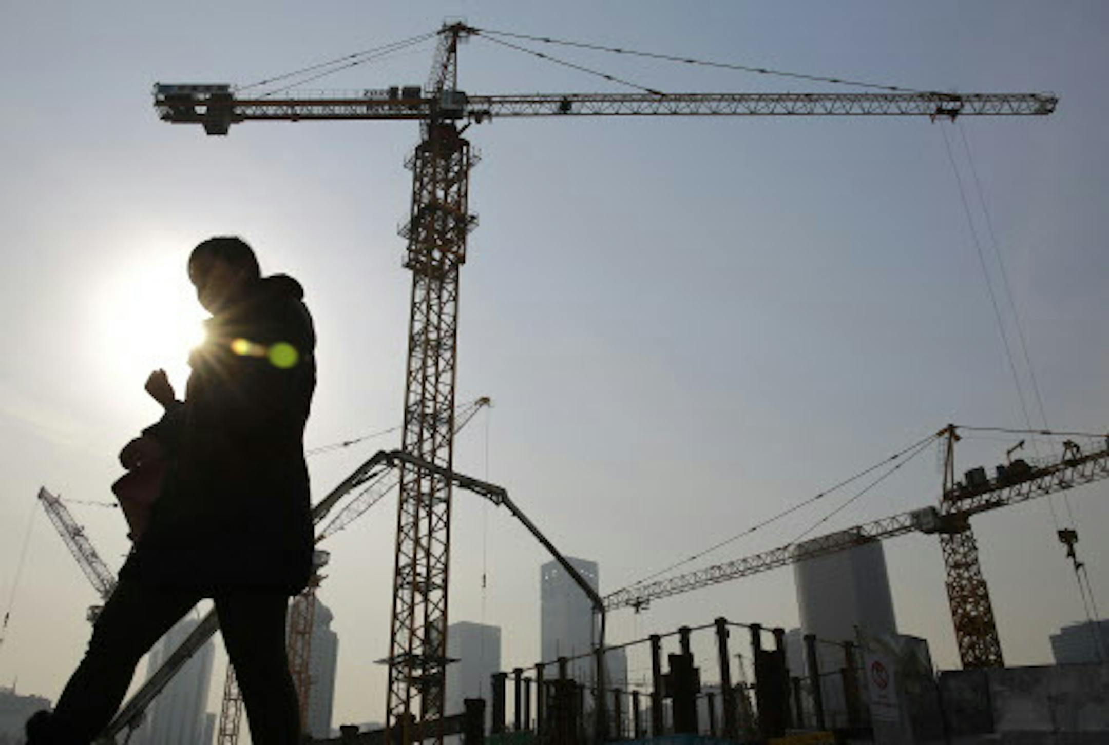 A woman walks past a construction site at the Central Business District of Beijing, China Tuesday, Jan. 20, 2015. China's economic growth slowed to 7.4 percent last year, the weakest expansion in more than two decades. The numbers released Tuesday are still miles ahead of growth rates in major industrialized economies, but represent a sharp decline from double digit growth in previous years. That adds to pressure on the country's communist leaders as they try to prevent a sharper slowdown in 201