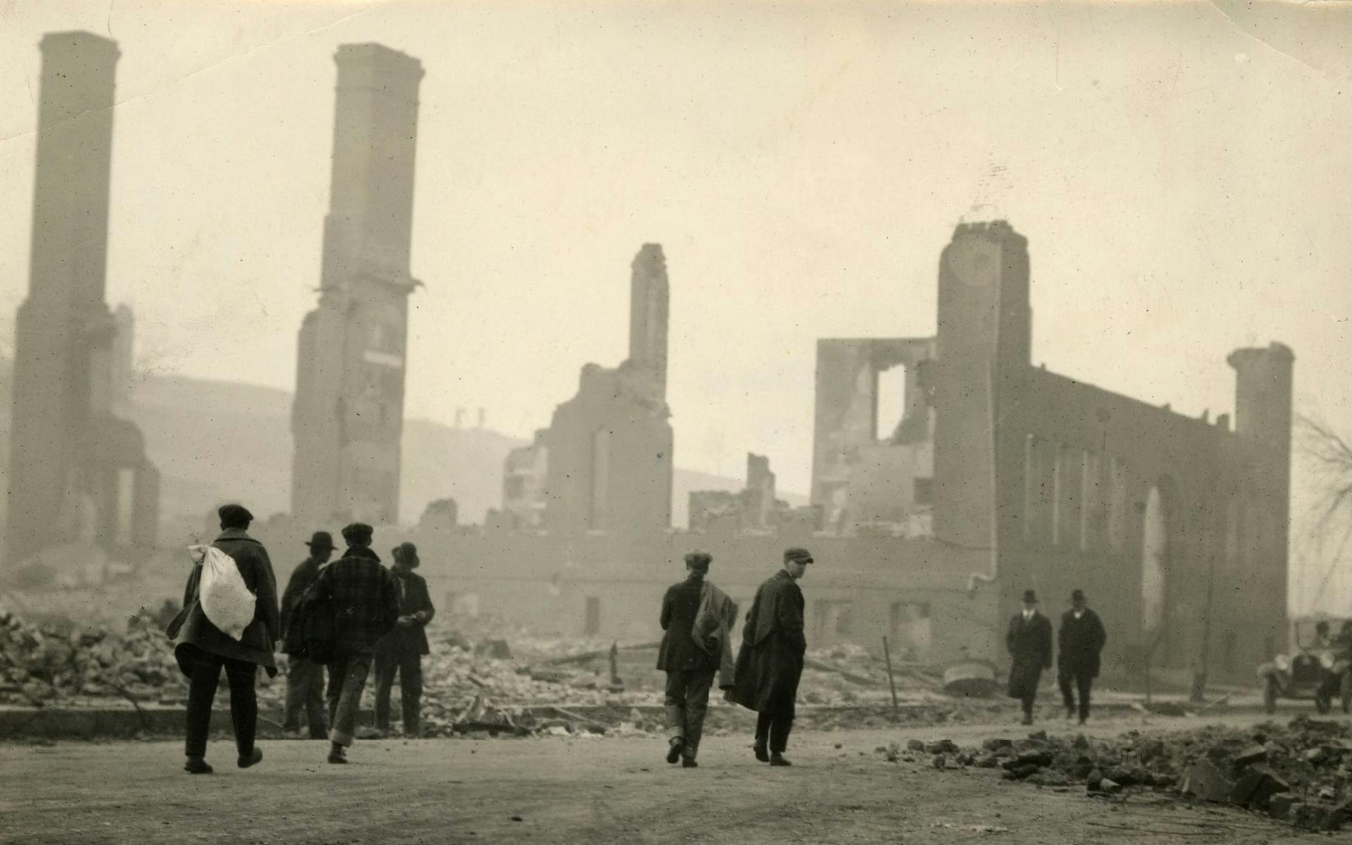People walking in front of a destroyed school building after the fires of 1918.
