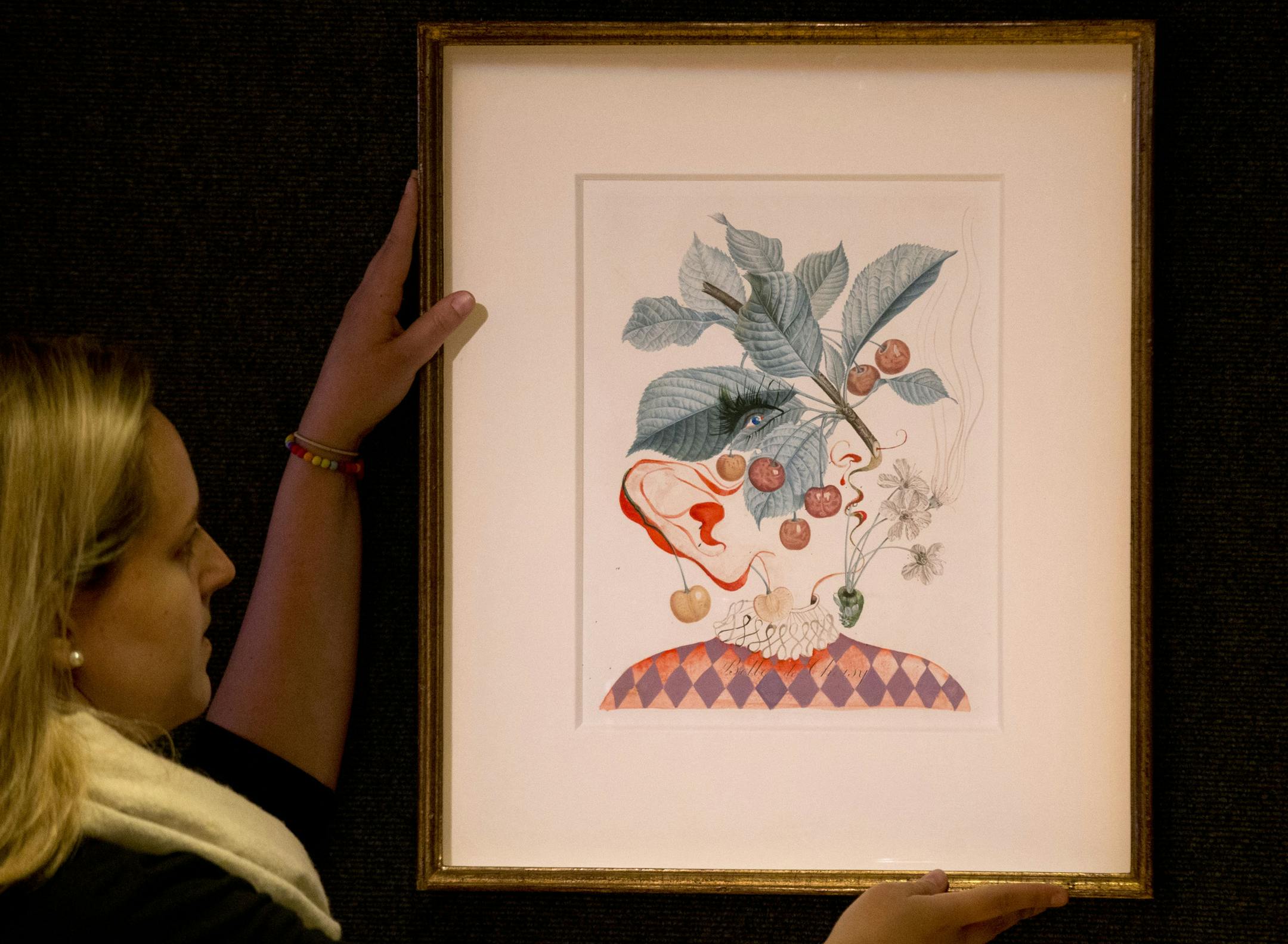 A Bonhams auction house employee poses for photographs with the Salvador Dali piece "Cerises Pierrot" (Pierrot Cherries), a watercolor, gouache and 19th century stipple engraving, at the company's premises in London, Wednesday, June 12, 2013. The painting, which is estimated to fetch 40,000 to 60,000 pounds ($62,597 to $93,896 / 47,171 to 70,756 euro) is one of a series of 14 works by the late Spanish artist called "The FruitDali Watercolours" that will feature in a sale of impressionist and mod