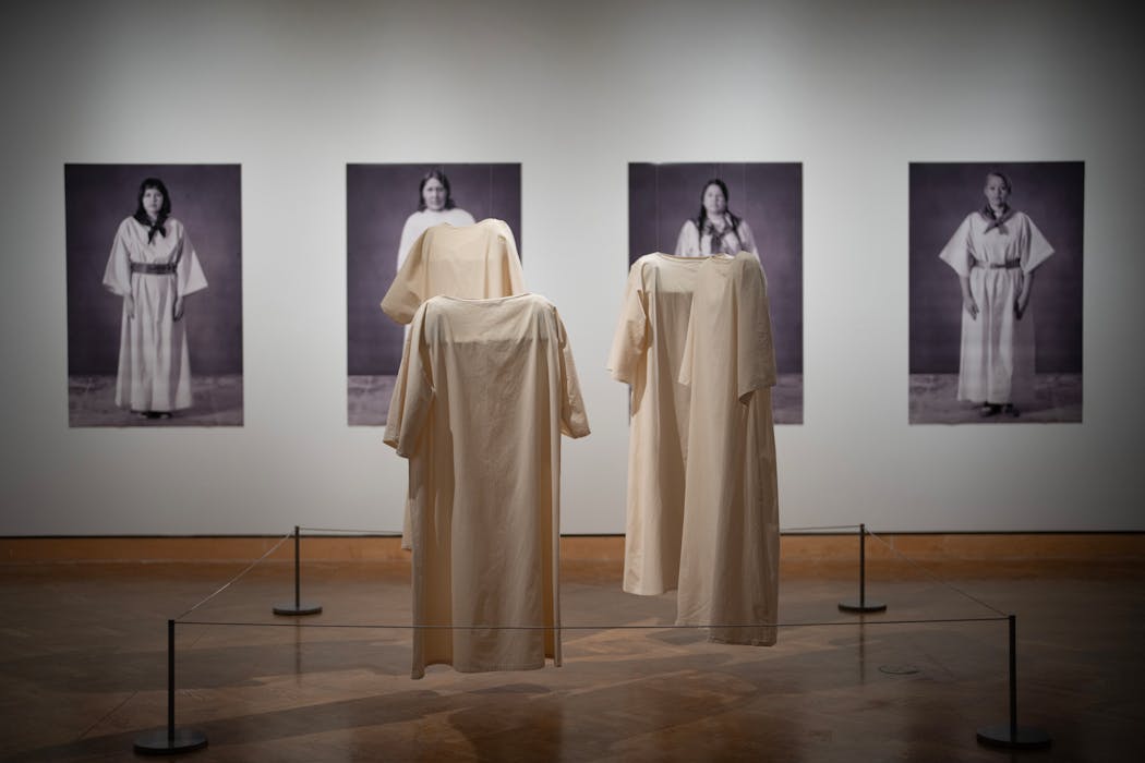 Four photographs by Faye HeavyShield, an interdisciplinary artist from Káínaa Nation, stand beside four canvas dresses, a work called “The Grandmothers.”