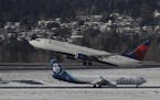 A Delta Air Lines plane takes off above a taxiing Alaska Airlines plane, Tuesday, Feb. 5, 2019, on a snow-bordered runway at Seattle-Tacoma Internatio