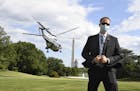 A U.S. Secret Service agent, wearing a mask to protect against COVID-19, stands on the South Lawn as Marine One lifts off with President Donald Trump,