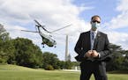A U.S. Secret Service agent, wearing a mask to protect against COVID-19, stands on the South Lawn as Marine One lifts off with President Donald Trump,