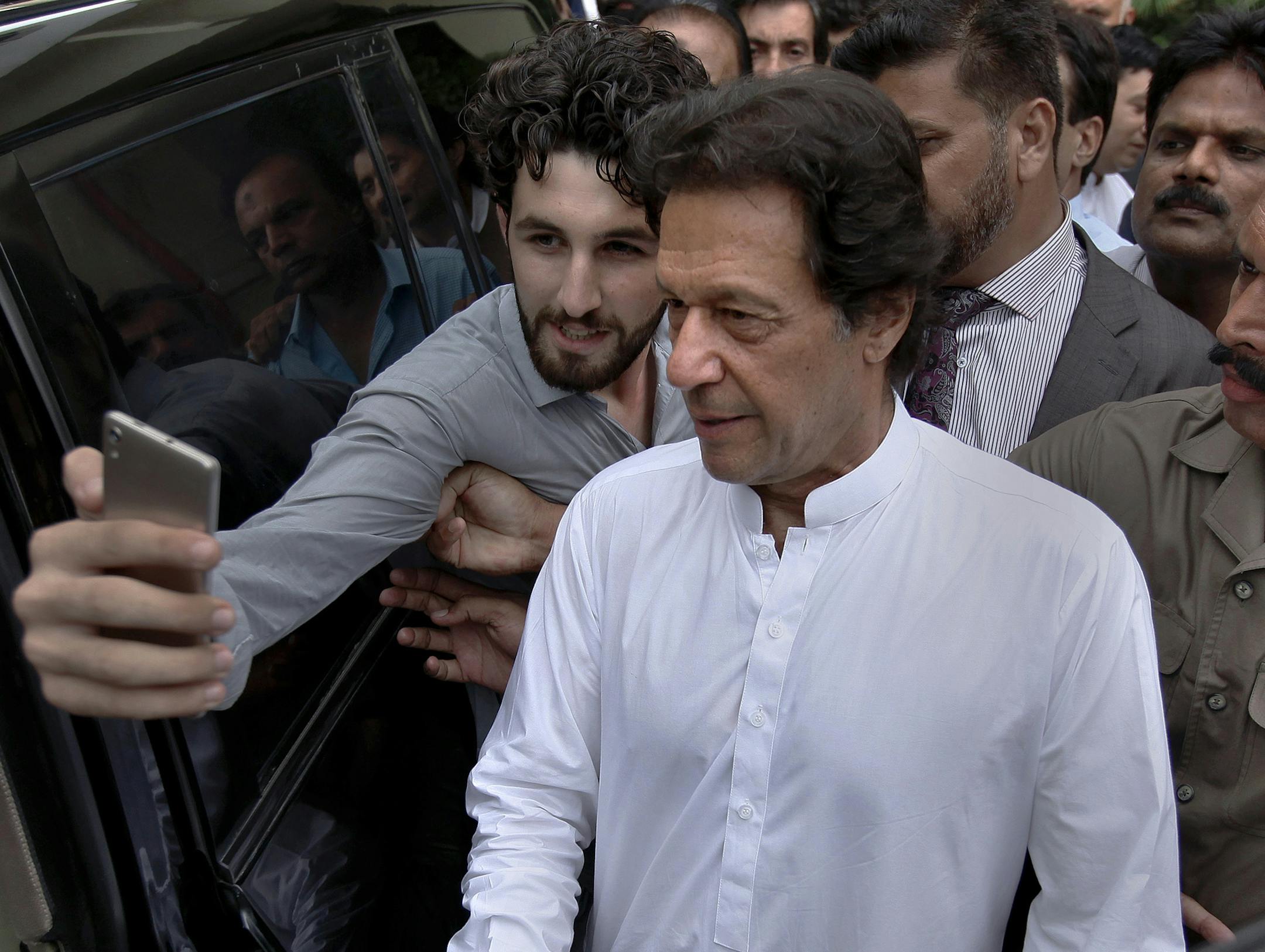 A Pakistani takes selfie with Imran Khan, center, head of the Pakistan Tehreek-e-Insaf party, as he leaves a party meeting in Islamabad, Pakistan, Monday, Aug. 6, 2018. The party won the most parliament seats in last month's general elections and is expected to form a governing coalition later this month. (AP Photo/Anjum Naveed) ORG XMIT: ANJ102