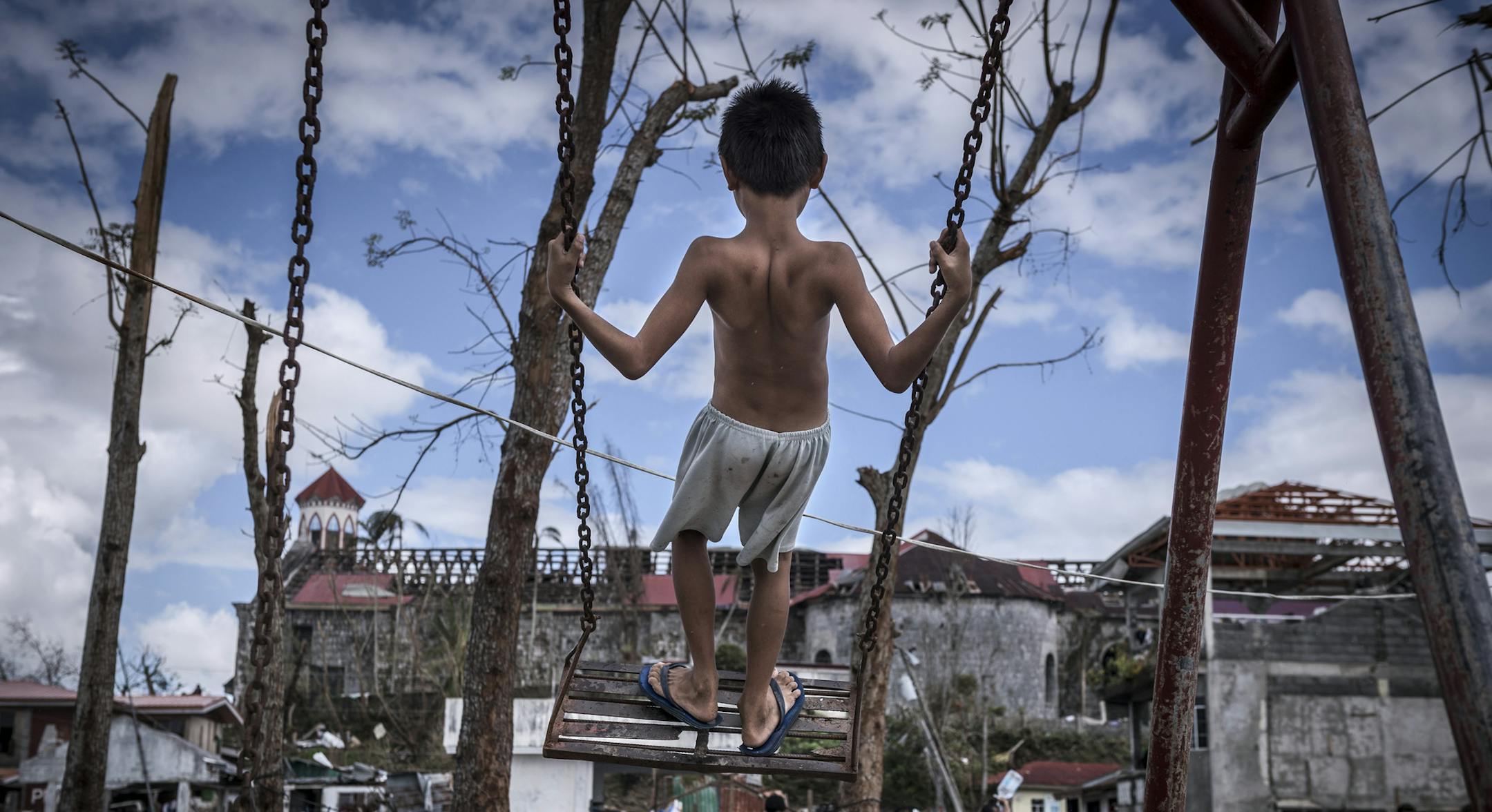 FILE -- A boy swings in front of St. Michael the Archangel Church surrounded by debris from Typhoon Haiyan in Basey, Samar province, Philippines, Nov. 18, 2013. (Sergey Ponomarev/The New York Times)