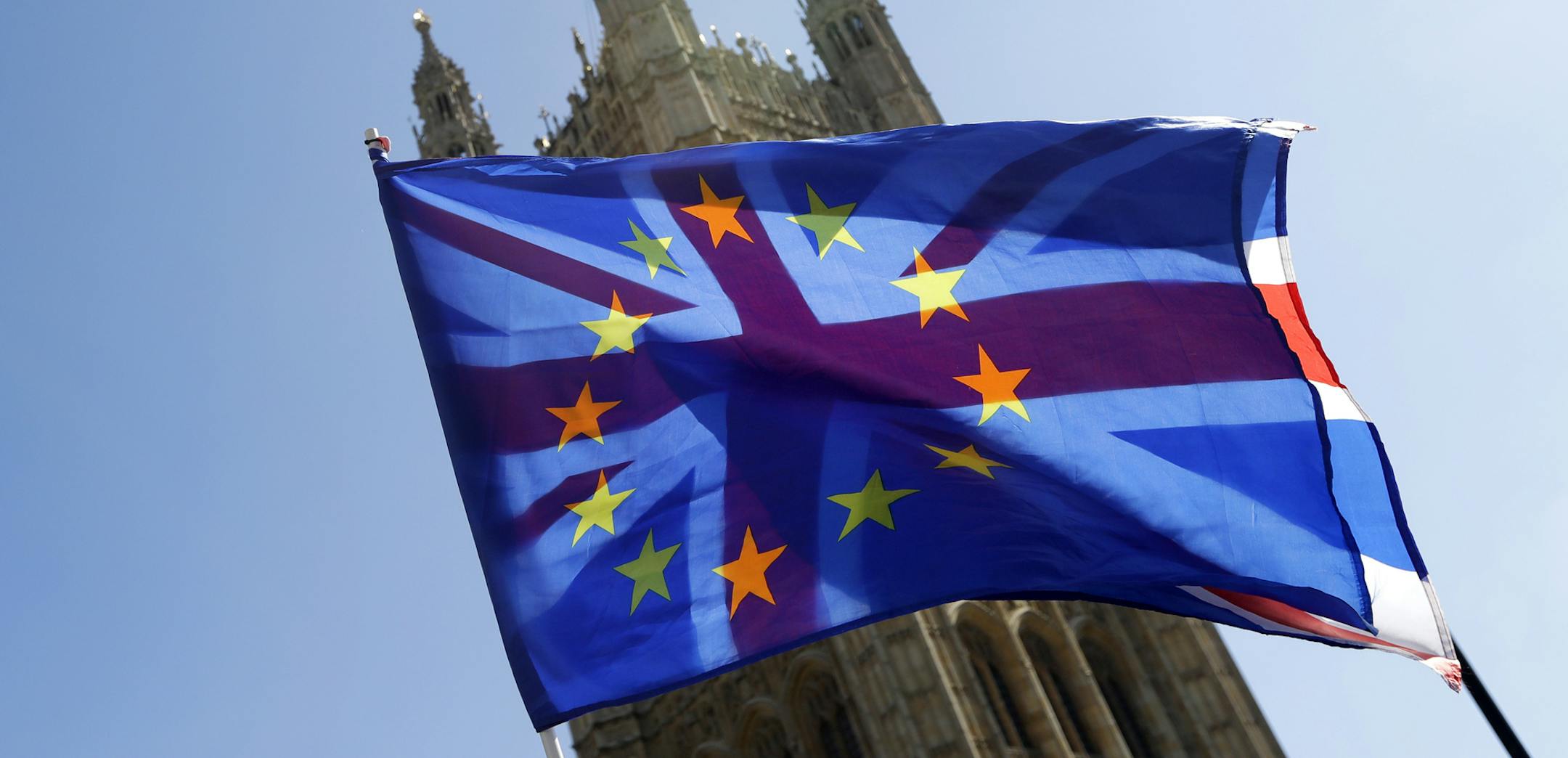 A British Union flag is flown behind a European Union flag, backdropped by Parliament in London, Wednesday, April 10, 2019. Just days away from a no-deal Brexit, European Union leaders meet Wednesday to discuss granting the United Kingdom a new delay to its departure from the bloc. (AP Photo/Kirsty Wigglesworth)