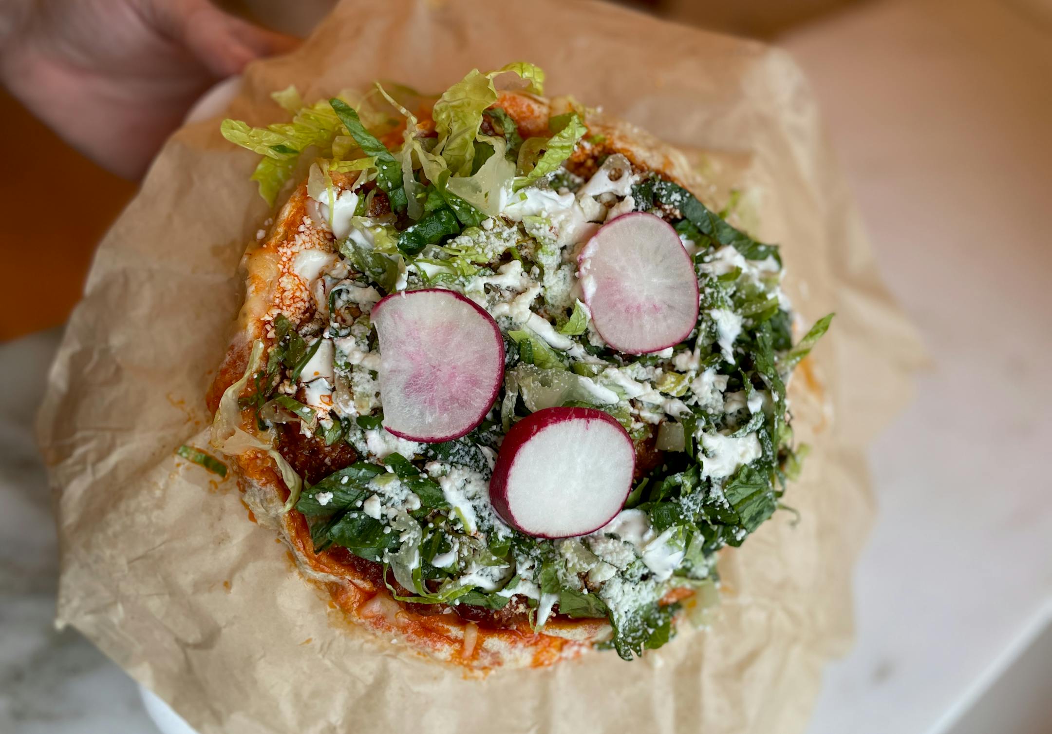 A sope topped with red chile braised pork, shredded lettuce, cotija cheese and sliced radishes.