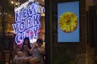 In this Thursday, July 5, 2018 photo, girls sit in front of an American cosmetics brand's shop window display reading "Greetings from New York City" a