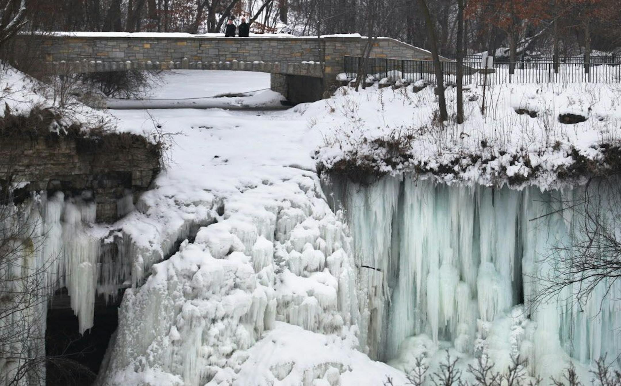 The falls at Minnehaha Falls is encrusted in ice but work by he Minnehaha Creek Watershed District and the U.S. Army Corps of Engineers has resumed to repair crib walls, bridges and retaining walls and is expected to be finished sometime this year.. In this photo:] The falls is frozen below as pedestrians cross the bridge over the creek, just above the falls.