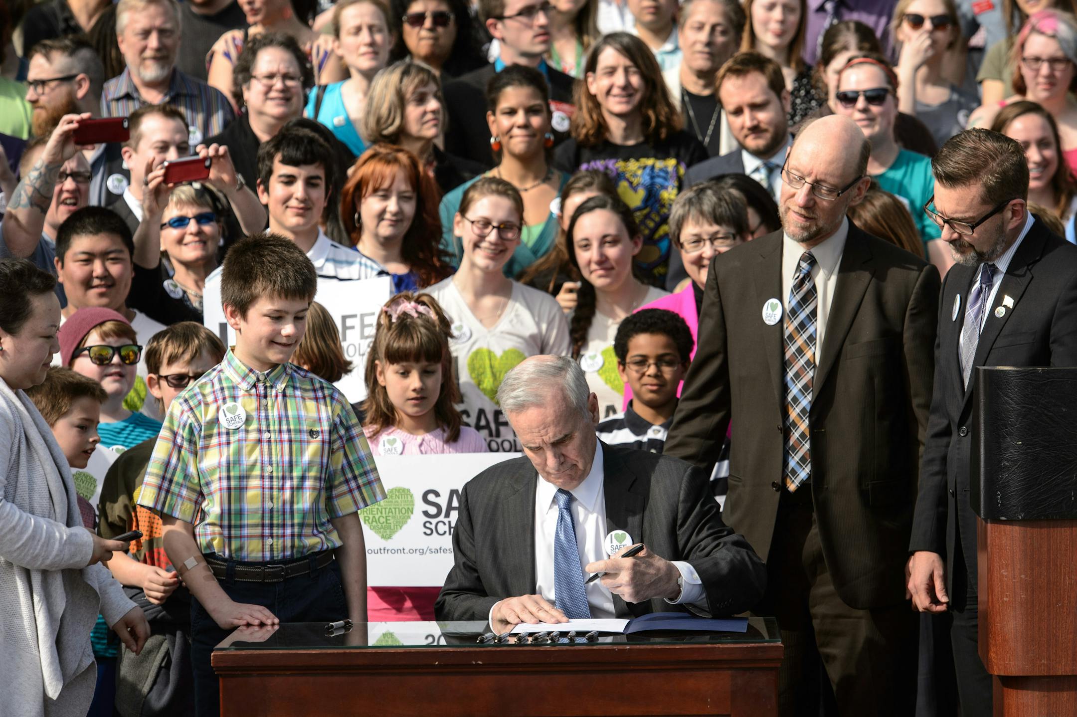 Gov. Mark Dayton signed the Safe and Supportive Schools Act on the steps of the Minnesota State Capitol on Wednesday, April 9, 2014. Sponsors of the anti-bullying bill, State Rep. Jim Davnie and State Sen. Scott Dibble are pictured on the right with Boy Scout Jake Ross, 11, left.