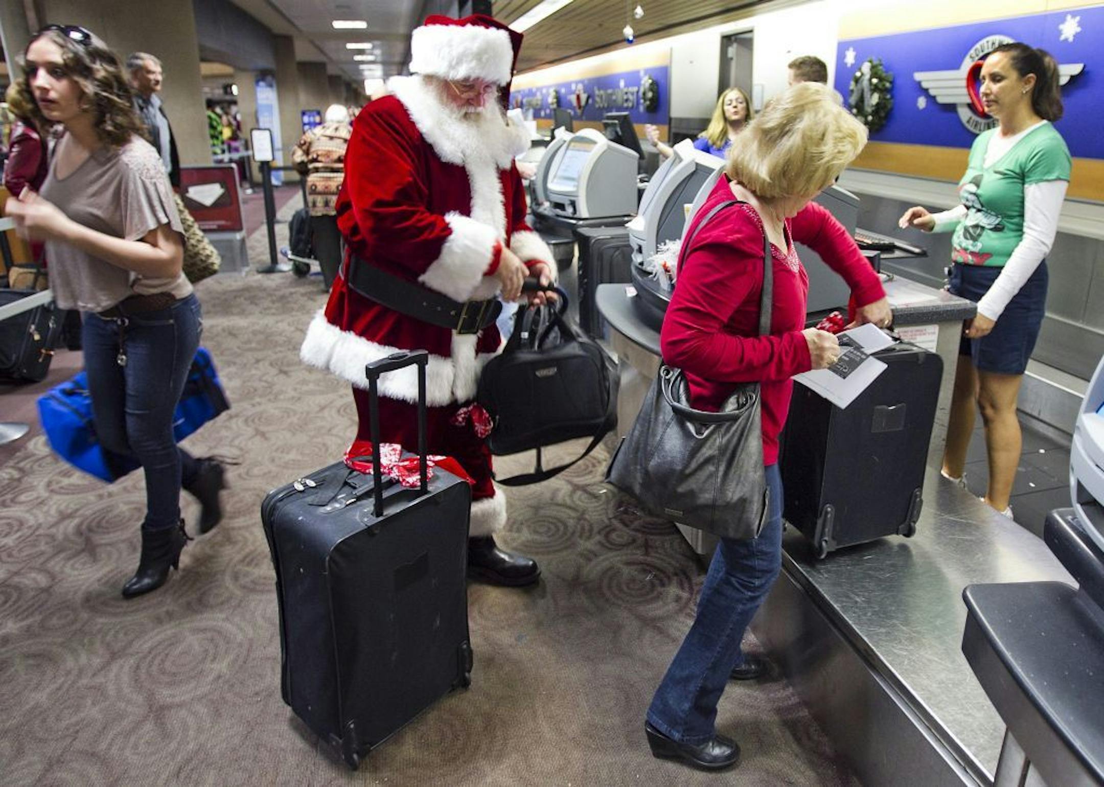 FILE - In this Wednesday, 21, 2011, file photo, holiday travelers, including Donald Occimio of Mesa, Ariz., dressed as Santa Claus, and his wife Diane check in with customer service agent Angelee Arciniega, right, for their Southwest Airlines flight at the Terminal 4 ticketing area at Sky Harbor International Airport, in Phoenix. The 2012 Christmas travel season could be the busiest in six years, with AAA predicting that 93.3 million Americans will hit the road. That's 1.6 percent more than last