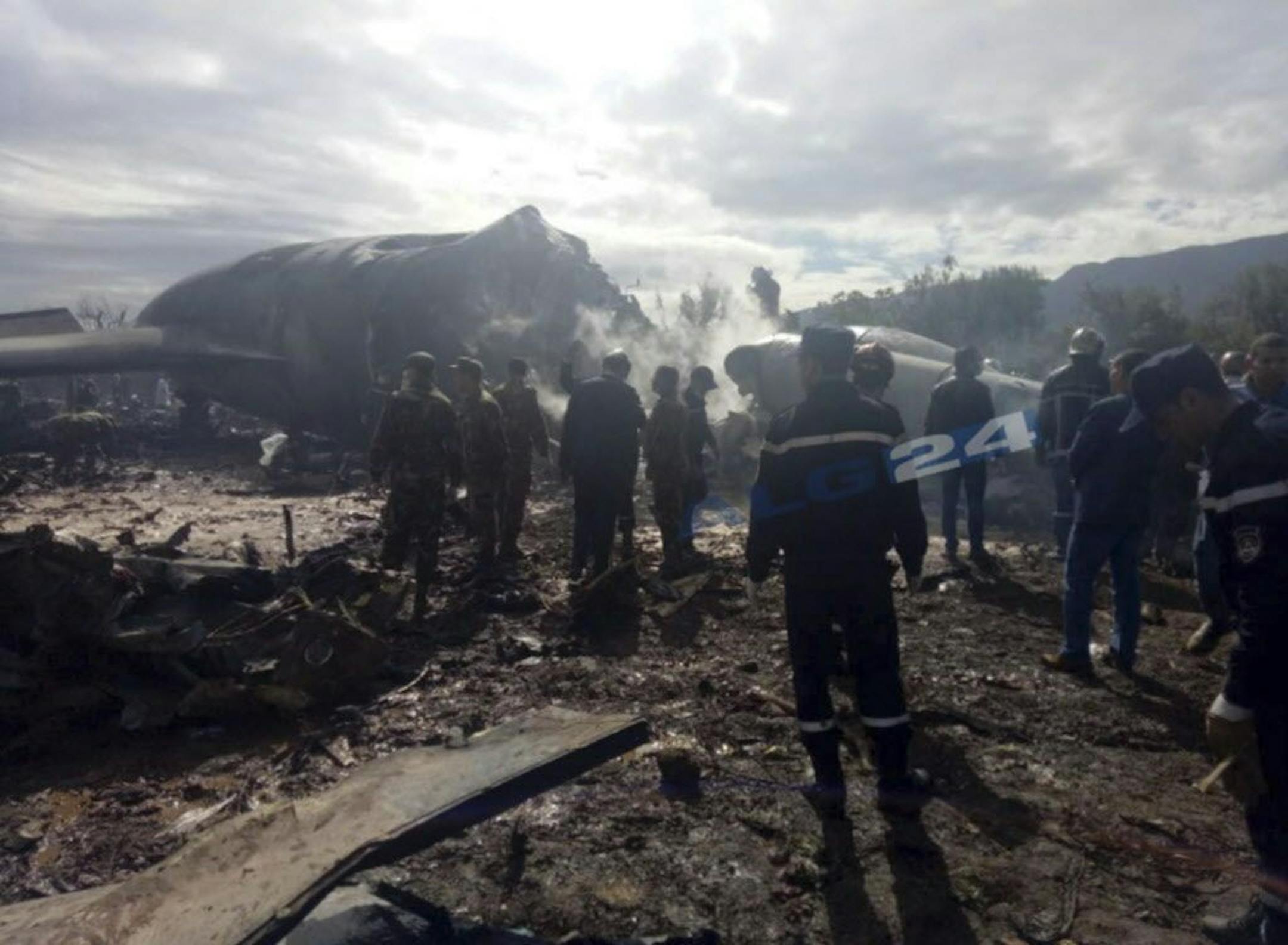 This image dated Wednesday, April 11, 2018, and posted by Algerian news agency ALG24, shows firefighters and soldiers at the scene of a fatal military plane crash near Boufarik military base near the Algerian capital, Algiers. (ALG24 logo placed on photo at source.)