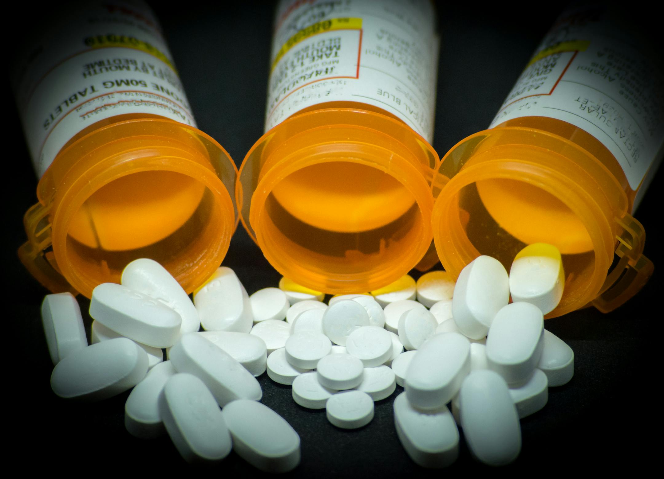 A variety of prescription pills lie in front of their respective bottles.