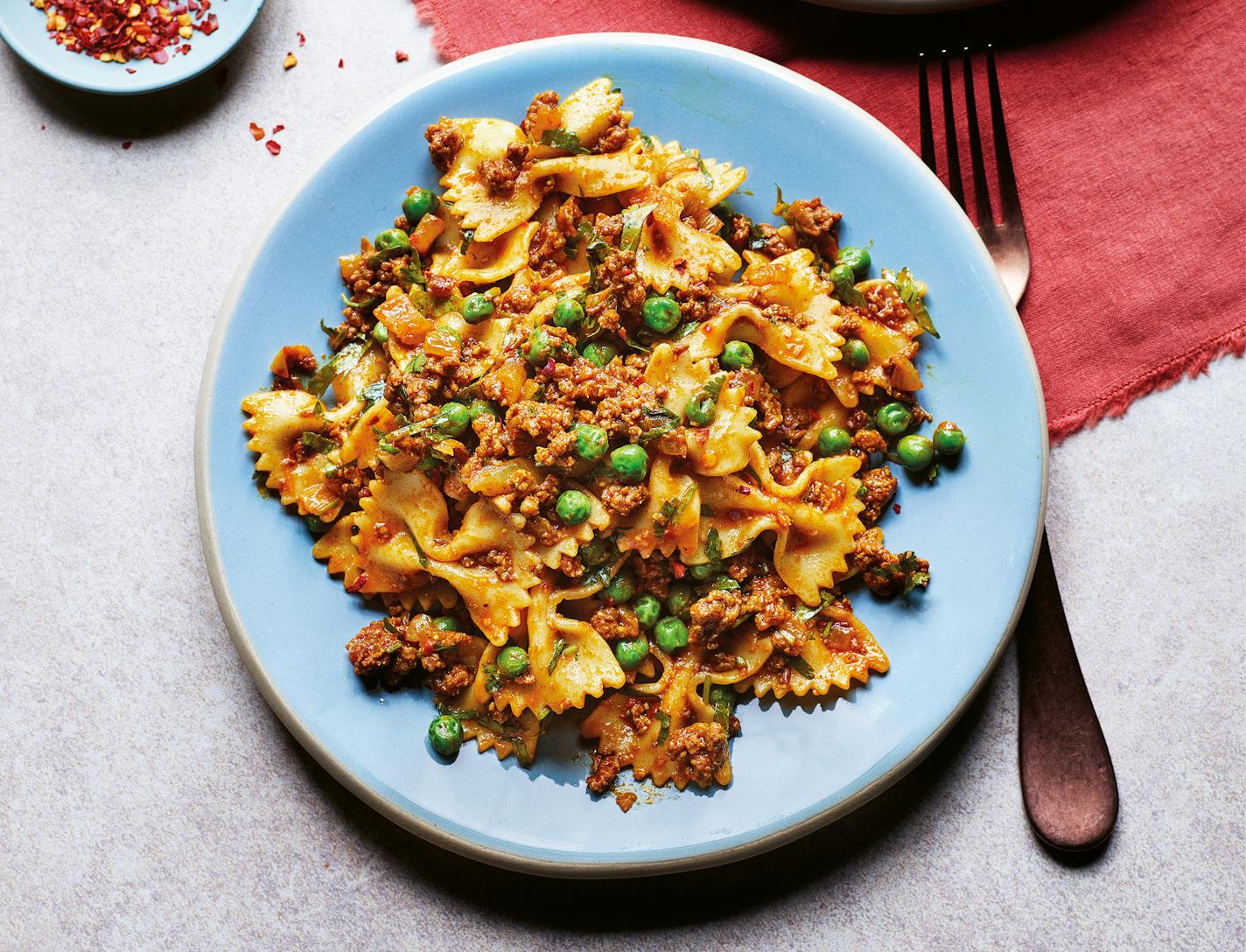 A light blue plate with Samosa Pasta -- bowtie pasta with hamburger, peas and flavorful spices.