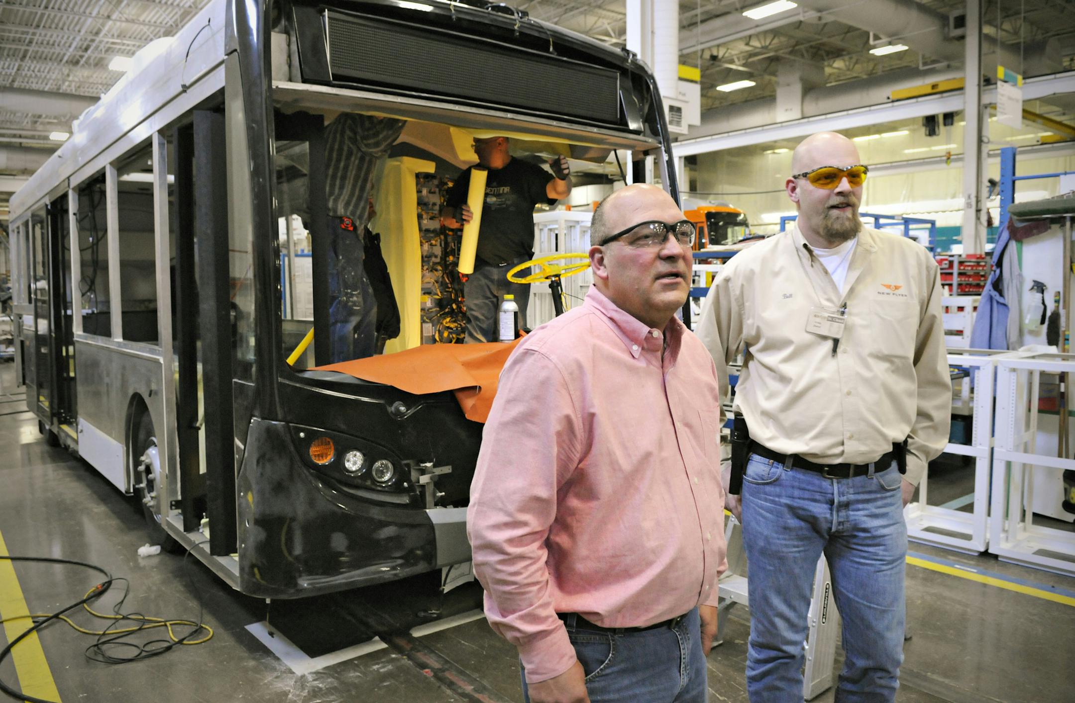 In this Friday, April 4, 2014 photo, New Flyer Industries Plant Manager David Bendorf, left, and Craig "Bull" Ziebol, Weld and MiDi Project Supervisor, talk about the new MiDi bus line with the first one to be produced behind them in St. Cloud, Minn. The MiDi is the company's first collaboration with another company, Alexander Dennis Ltd. of Scotland. (AP Photo/St. Cloud Times, Jason Wachter)