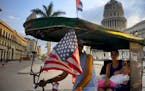 A taxi pedals his bicycle, decorated with Cuban and U.S. flags, as he transports a woman holding a sleeping girl, near the Capitolio in Havana, Cuba, 