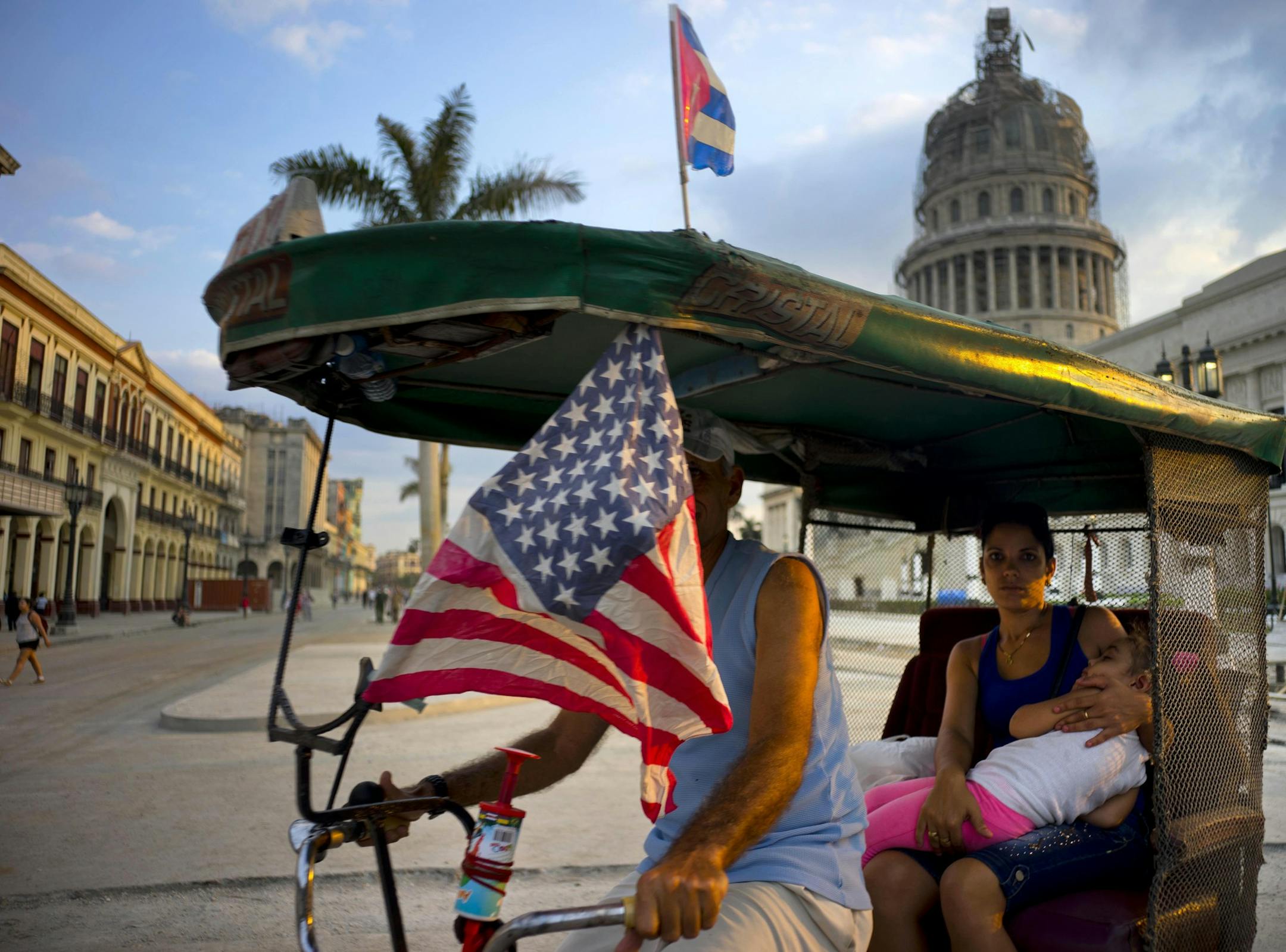A taxi pedals his bicycle, decorated with Cuban and U.S. flags, as he transports a woman holding a sleeping girl, near the Capitolio in Havana, Cuba, Tuesday, March 15, 2016. President Barack Obama will travel to Cuba on March 20. (AP Photo/Ramon Espinosa)