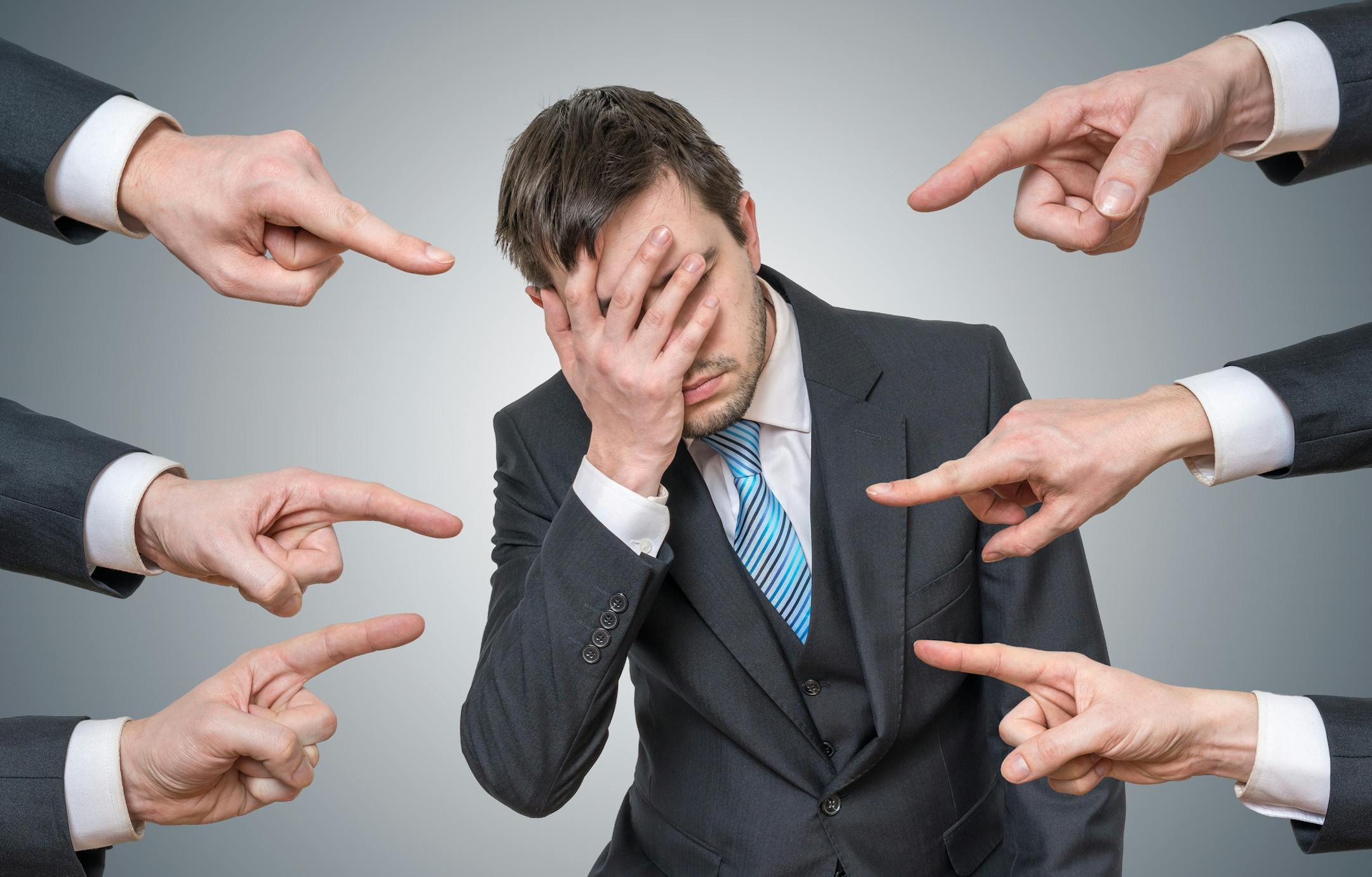 Many hands are pointing at man and blame him.