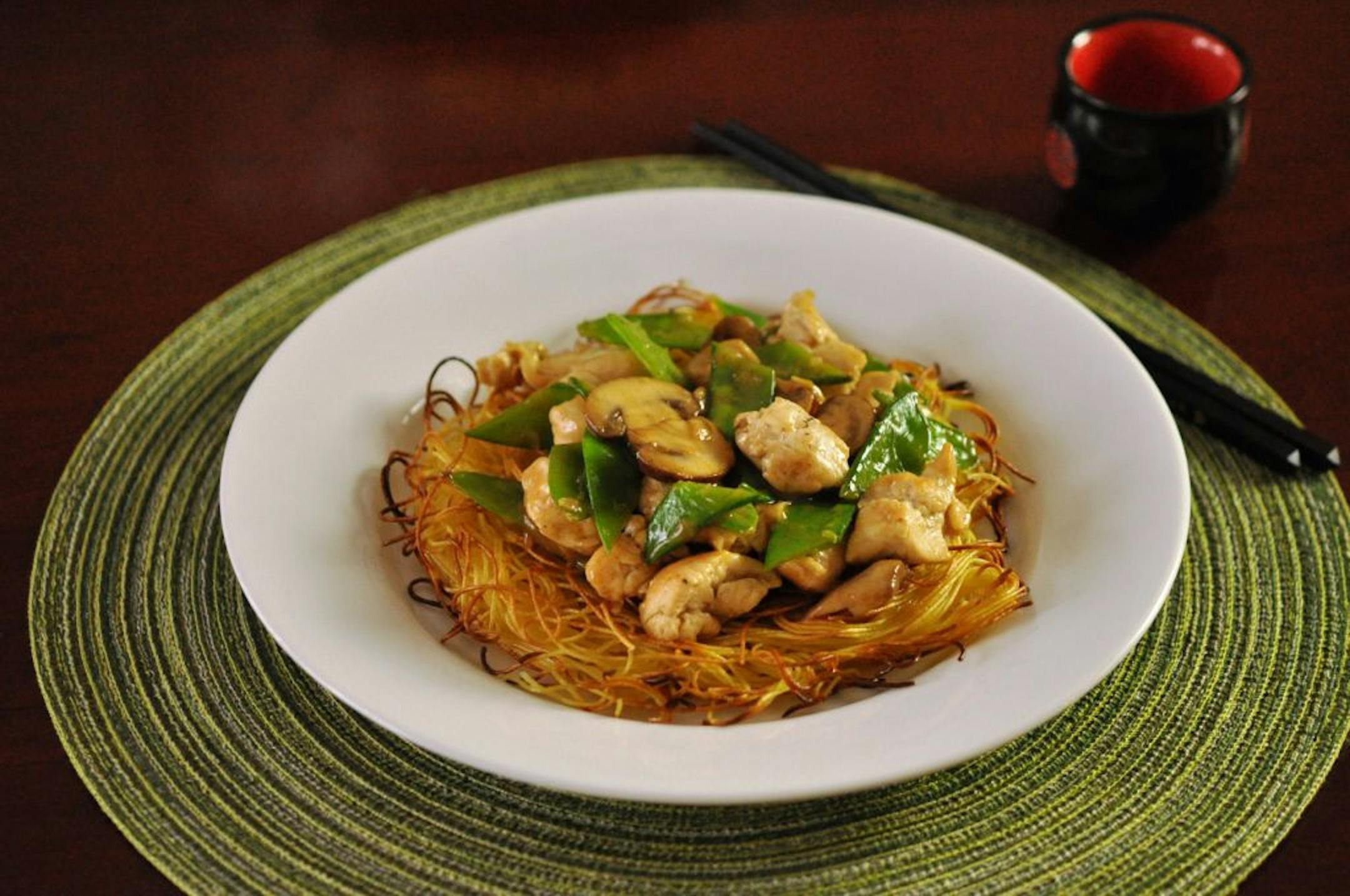 Pea pods and chicken are served over a bed of crisp noodles.