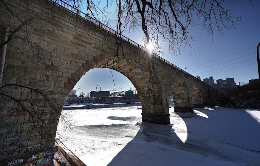 The late afternoon sun cast graphic shadows through the Stone Arch Bridge, across ice covering the Mississippi River.