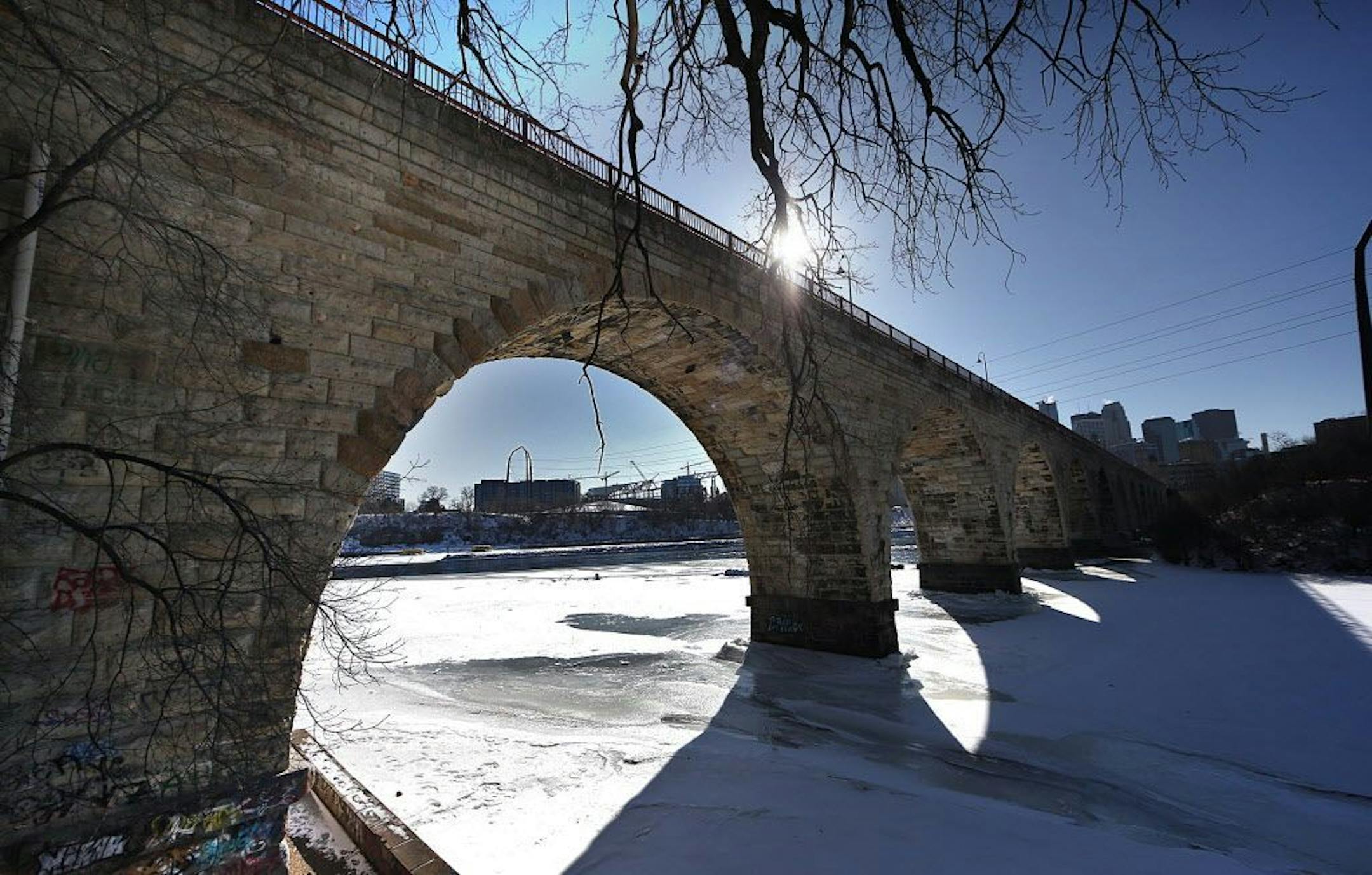 The late afternoon sun cast graphic shadows through the Stone Arch Bridge, across ice covering the Mississippi River.