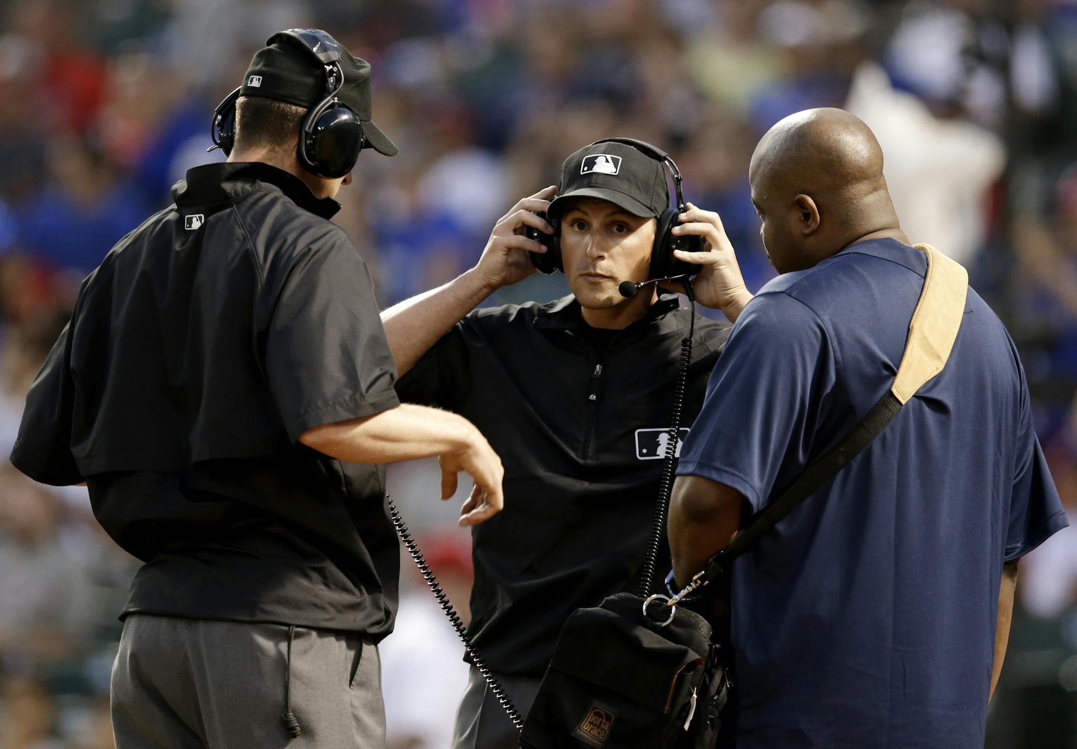 First base umpire Quinn Wolcott, center, removes his headset after an instant replay review in the second inning of a spring exhibition baseball game between the Quintana Roo Tigres, of Mexico, and the Texas Rangers, Thursday, March 27, 2014, in Arlington, Texas. Wolcott and the rest of the officials ruled a ball did clear the fence to give Rangers' Donnie Murphy a 3-run home run. (AP Photo/Tony Gutierrez) ORG XMIT: MIN2014032800194963