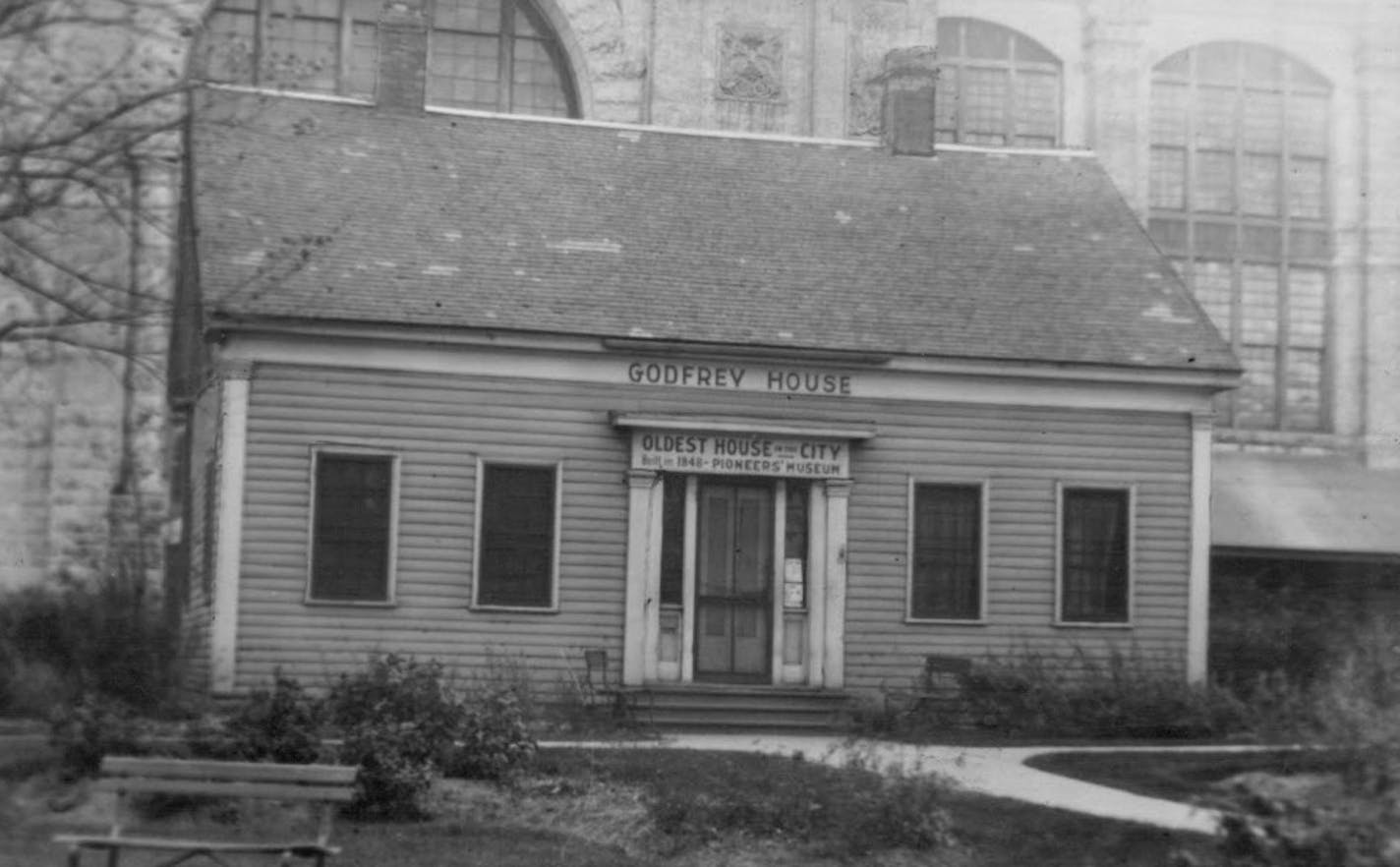 A 1921 image of the 1848 Ard Godfrey house, the oldest surviving house in the Twin Cities. The Industrial Exposition Building looms in the background.