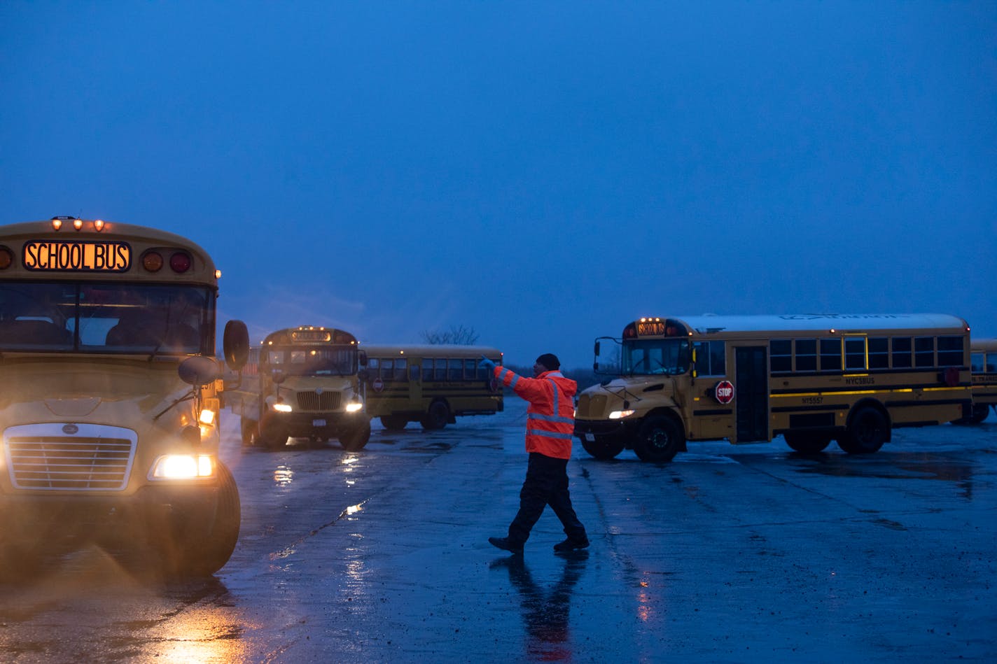 A worker directed school buses to line up at the tent complex used as a shelter for migrant families at Floyd Bennett Field in Brooklyn, on Jan. 9, 2024. New York City evacuated on Tuesday about 500 families with children — nearly 2,000 people in total — from a massive tent shelter set up on a desolate former airplane runway in southern Brooklyn ahead of heavy rains and wind expected to hit the area. (Kirsten Luce/The New York Times)