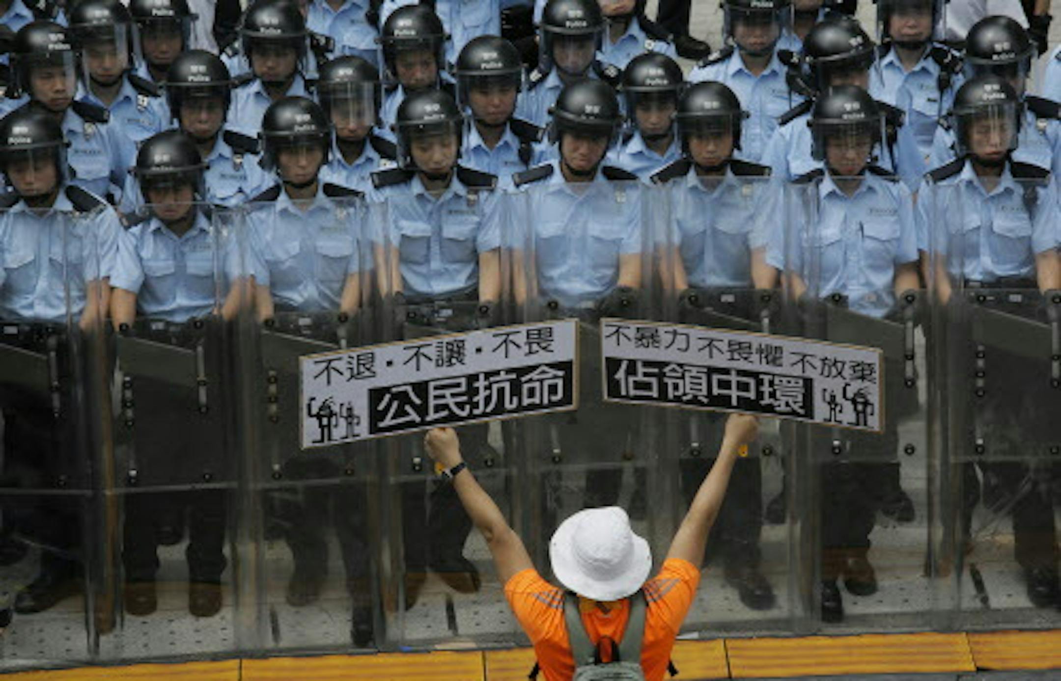 A protester raises placards that read "Occupy Central and Citizen Against Order" in front of riot policemen outside the government headquarter in Hong Kong, Saturday, Sept. 27, 2014. Riot police in Hong Kong on Saturday arrested scores of students who stormed the government headquarters compound during a night of scuffles to protest China's refusal to allow genuine democratic reforms in the semiautonomous region. (AP Photo/Vincent Yu)