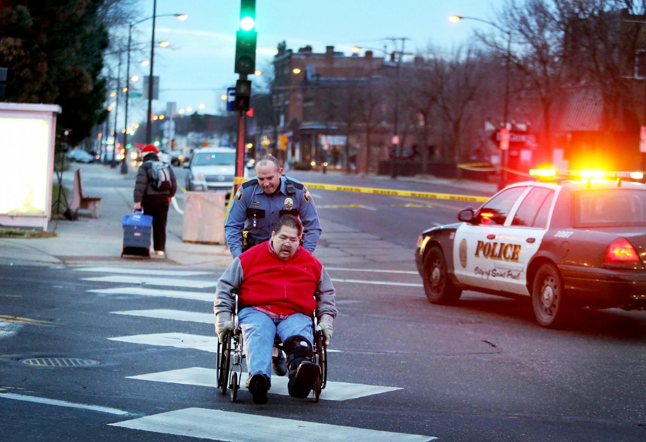 Scene of an early morning homicide where two persons are dead and a third critically wounded near the Salvation Army at 7th St and Smith Ave. Thursday, Dec. 10, 2015, in St. Paul, MN. Here, St. Paul police officer Reetz helps a man in a wheelchair cross Smith Ave. on 7th St.