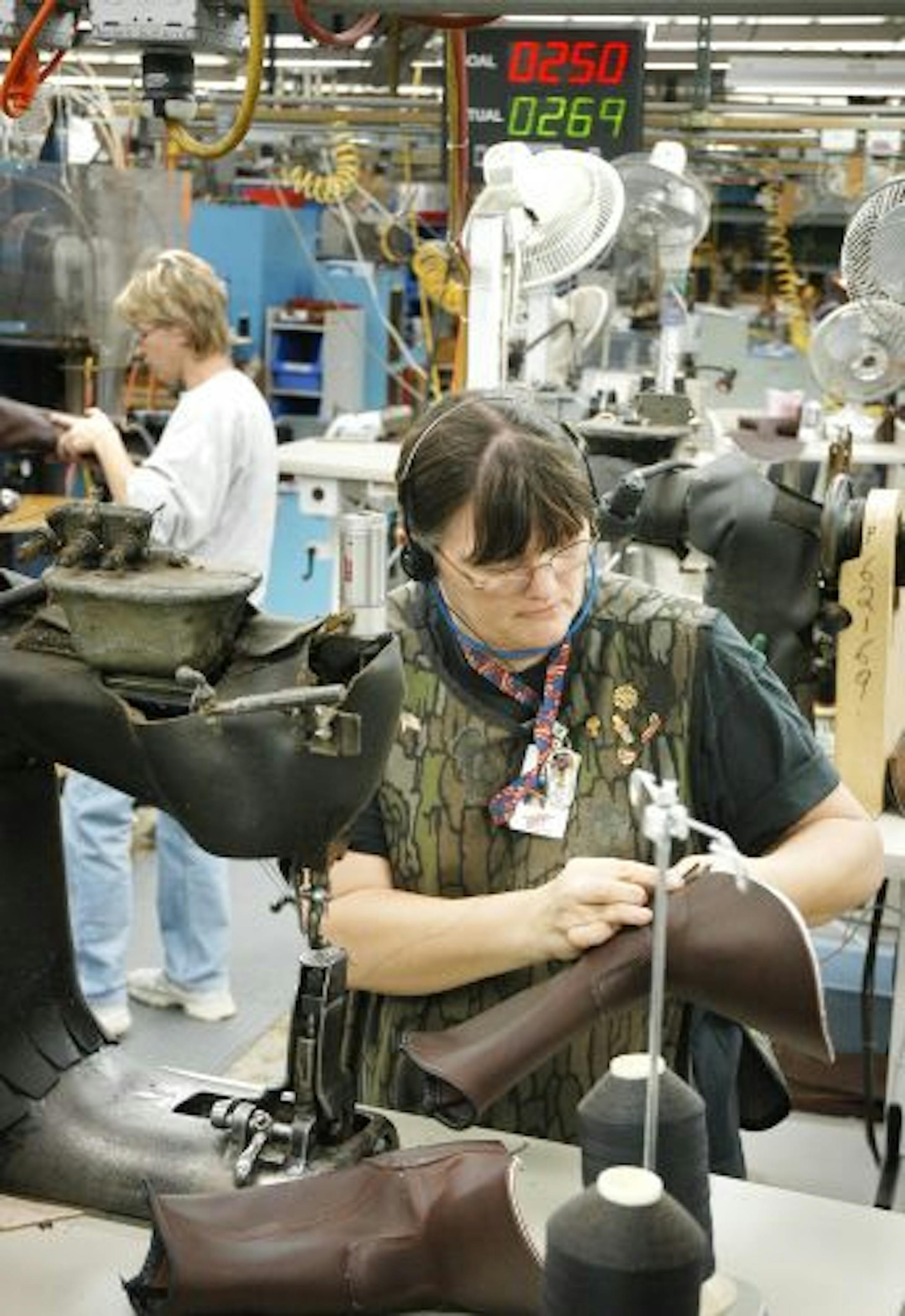 Glen Stubbe/Star Tribune Thursday, January 21, 2004 -- Red Wing, Minn. -- Peggy Hoyer assembles the leather uppers on boots at Red Wing Shoes, following the Toyota Sewing System method allowing workers to follow a shoe part through production. In the background is Vickie Keane. The top red number in the background is the goal number for this point in the shif of 250 shoe uppers, so far the team of four is exceeding their goal at 269. Peggy has been with the company since 1974.