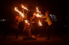 A group of dancers weave through the darkness with flaming hula hoops.