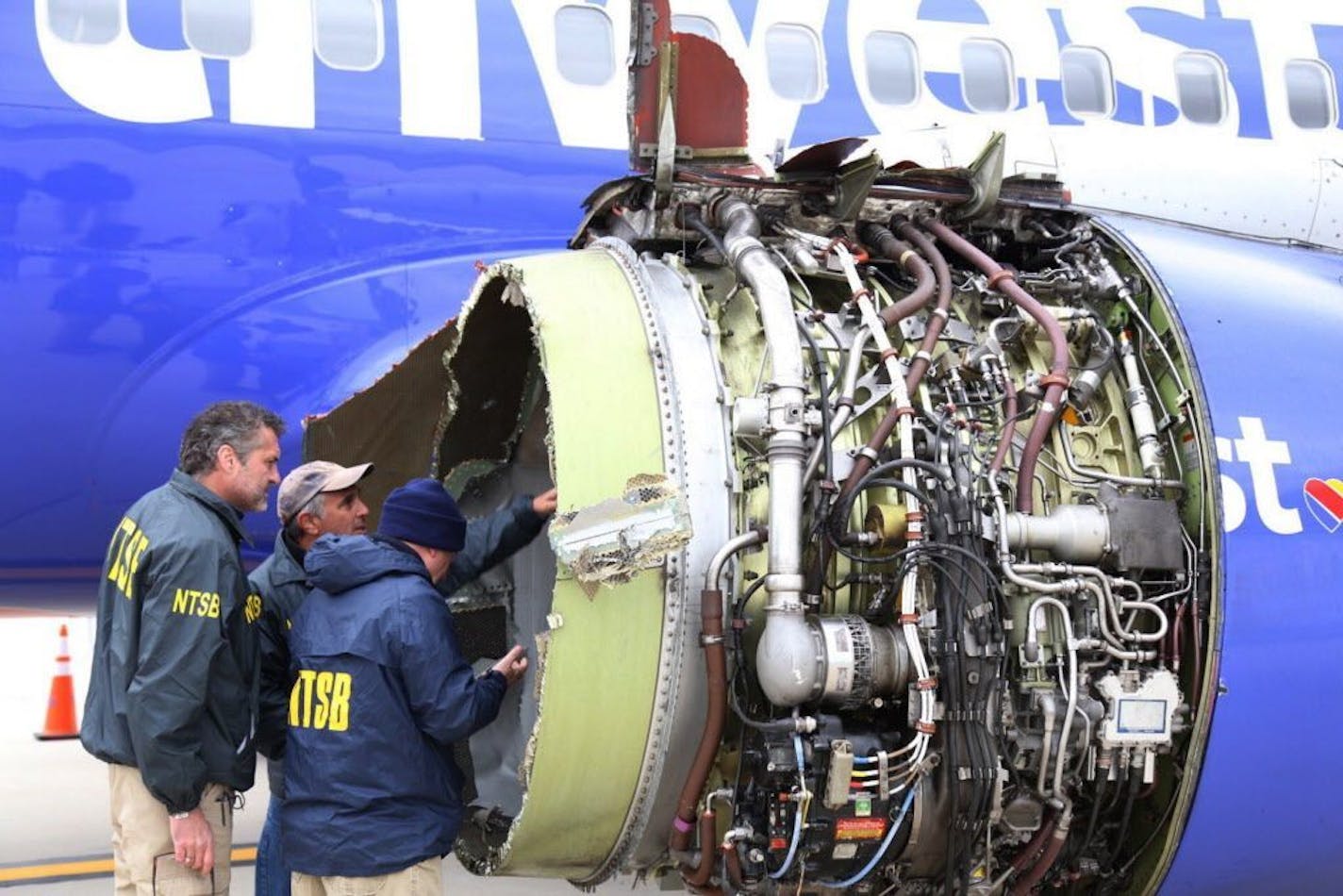 FILE- In this April 17, 2018, file photo National Transportation Safety Board investigators examine damage to the engine of the Southwest Airlines plane that made an emergency landing at Philadelphia International Airport in Philadelphia. In new accounts released Wednesday, Nov. 14, into the April accident, the flight attendants described being unable to bring the woman back in the plane until two male passengers stepped in to help. The flight attendants told investigators at least one of the me