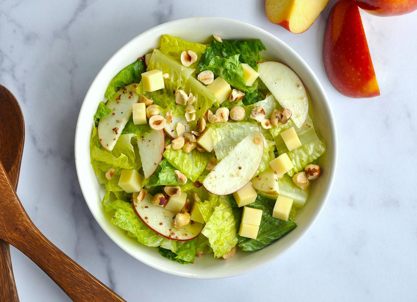 A white bowl filled with a salad made from romaine lettuce, apples, Gruyère and hazelnuts.