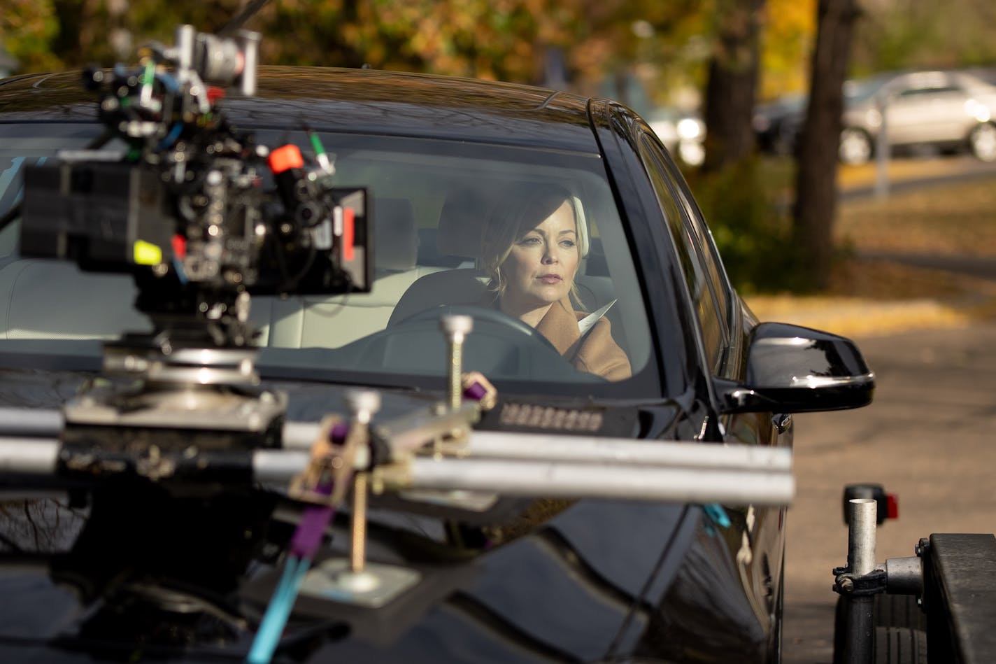 A photo of a woman driving a car, with a movie camera mounted on the hood.