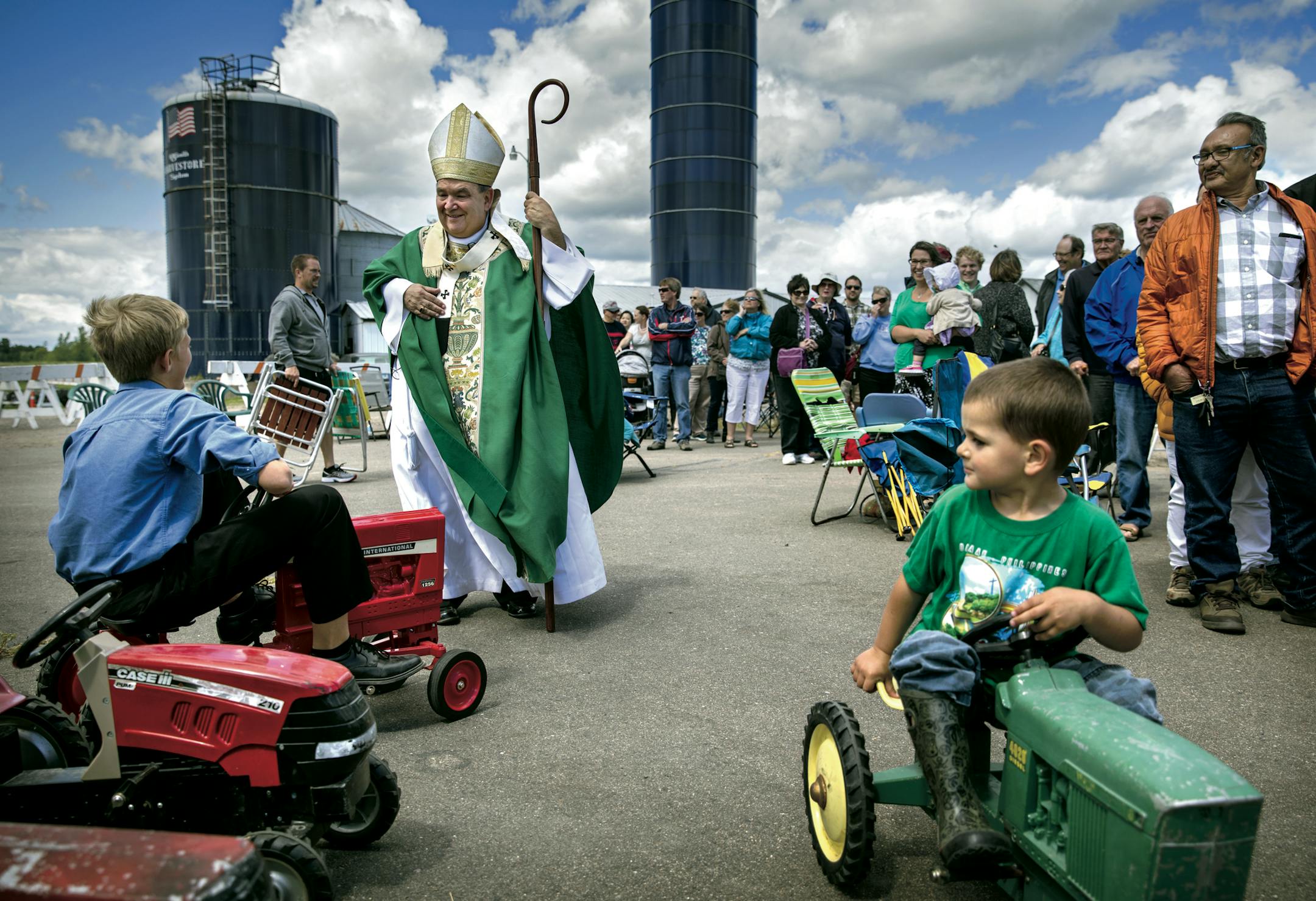 Archbishop Bernard Hebda is known for being an accessible bishop. Here, he chats with Simon Strand, 11, after the Rural Life Mass at the Dahlheimer farm in Center City, Minn. Gabe Pratt, 3, is at right.