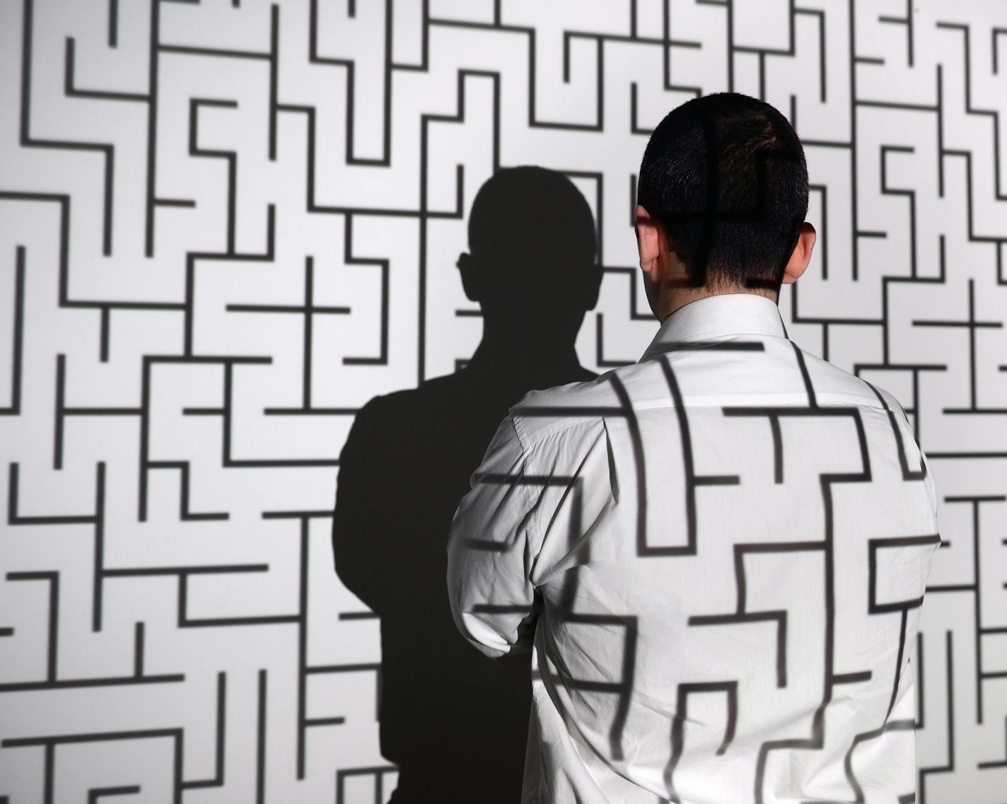 Businessman standing in front of projection screen. Projector reflects a labyrinth to screen and businessman's back.