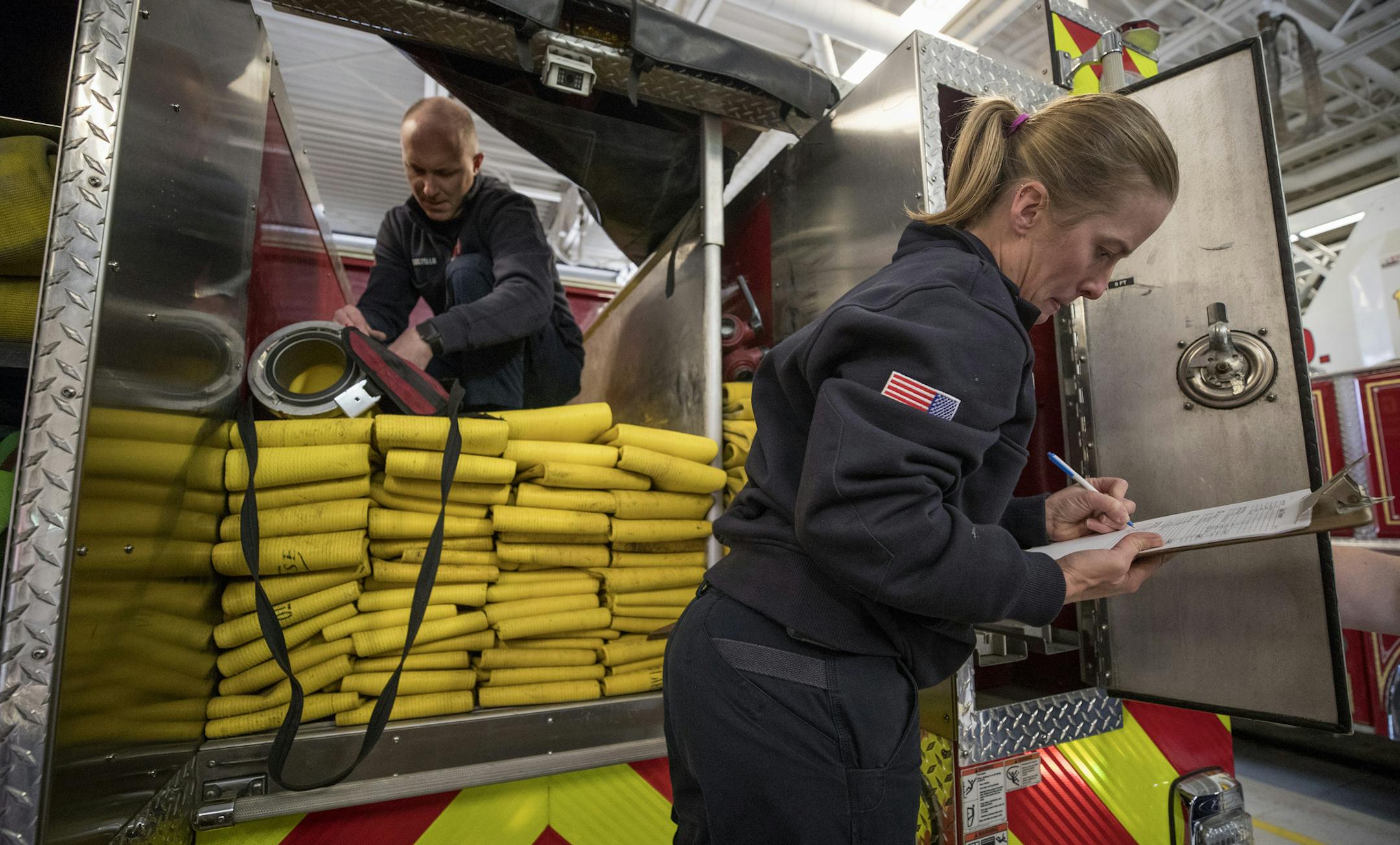 Debralyn Bryant, a volunteer firefighter, took notes as engineer Brian Costello packed up hoses in Inver Grove Heights. Many departments are struggling to fill their rosters.