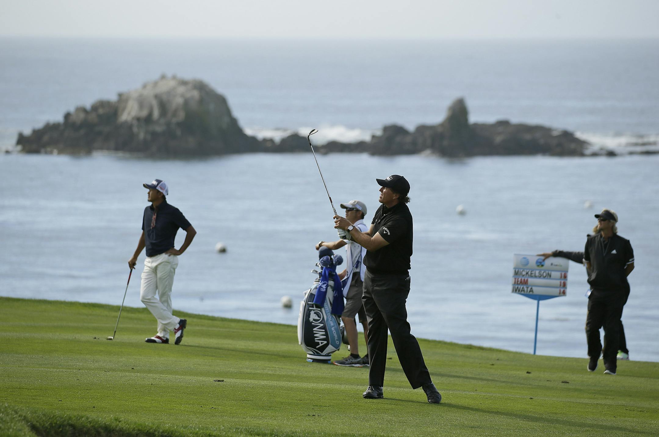 Phil Mickelson, foreground, follows his shot from the fourth fairway of the Pebble Beach Golf Links during the final round of the AT&T Pebble Beach National Pro-Am golf tournament Sunday, Feb. 14, 2016, in Pebble Beach, Calif. Hiroshi Iwata, of Japan, looks on. (AP Photo/Eric Risberg)