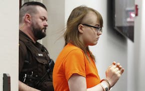 Sheriff's deputy escorts Morgan Geyser in handcuffs and orange jail T-shirt.