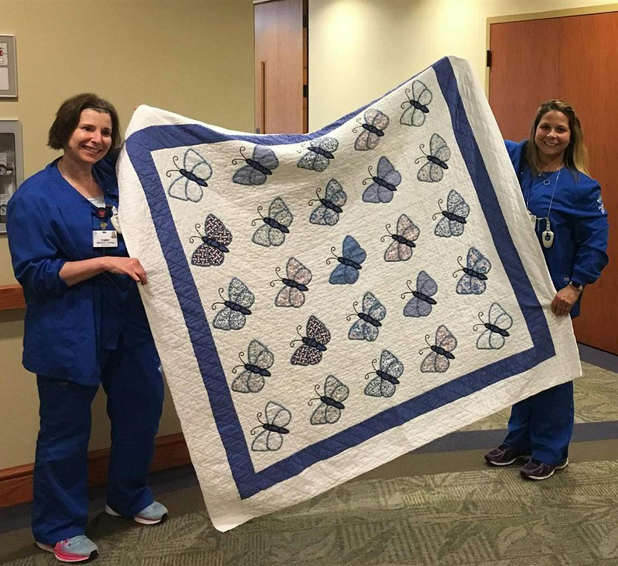 Tammy Wright, left, and Carrie Merk, hospice nursing assistants at the Medina Inpatient Hospice Care Center, hold up a quilt embroidered with butterflies that is used to cover deceased patients after they are bathed and before the funeral home arrives. The quilt was made and donated by volunteers and is meant to help soothe families who may be seeing loved ones for the last time. (Michael Ollove/Pew Charitable Trusts/TNS)