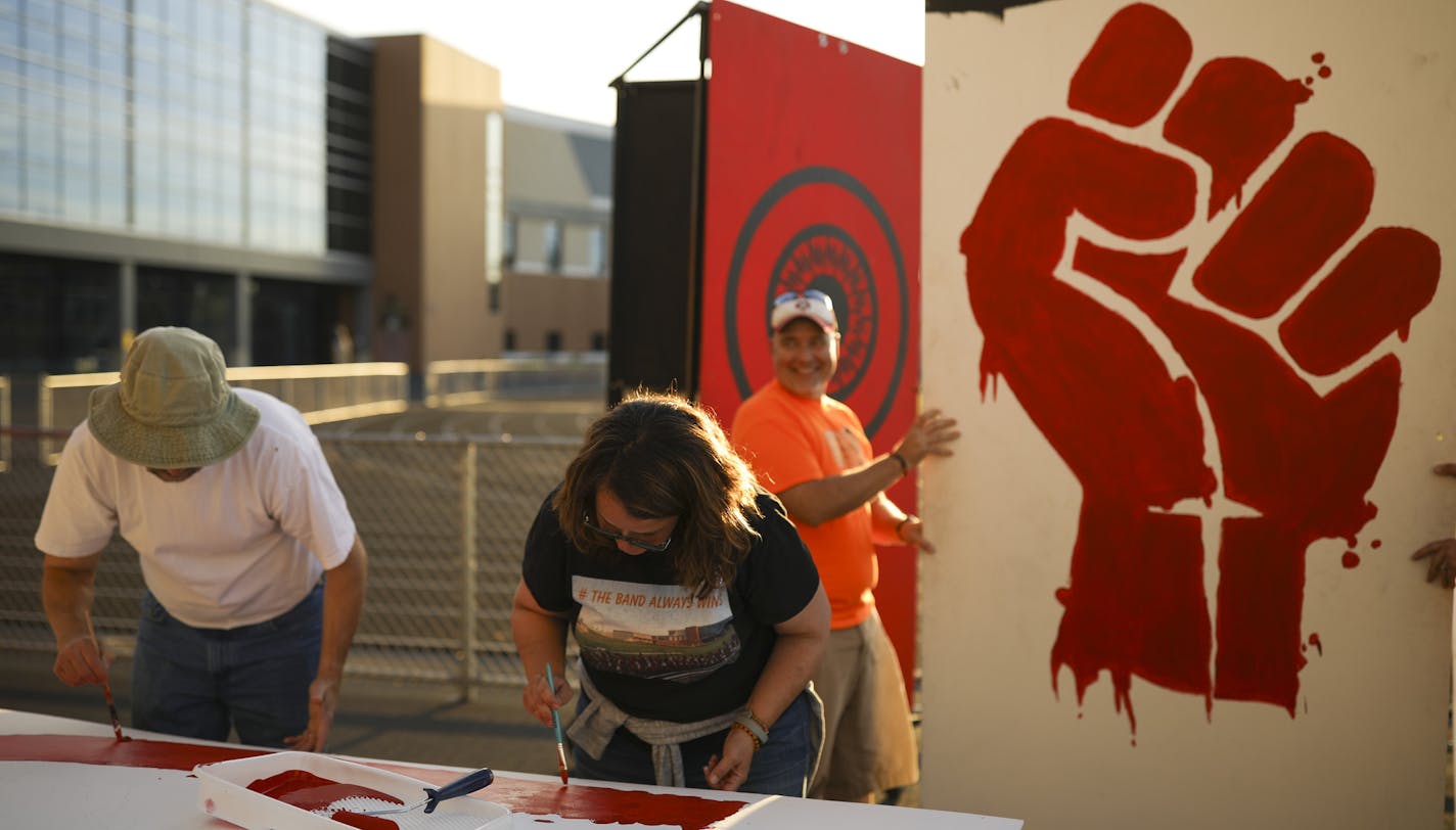 Parent volunteers Jason Viska and Nicole Colson painted a "U" a board that will be a part of the word "UNITE." Behind them, a clenched fist will be replaced by an image of two hands clasping. ] JEFF WHEELER &#xef; jeff.wheeler@startribune.com The Farmington High School marching band has had to revise their halftime program, "Dystopia" slightly after some thought it had political overtones. On Thursday night, the band's rehearsal incorporated the changes while parent volunteers painted new letter