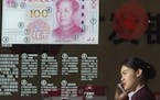FILE - In this Feb. 16, 2016 file photo, a woman speaks on her phone near a display highlighting the new Chinese bank notes at a bank in Beijing, Chin
