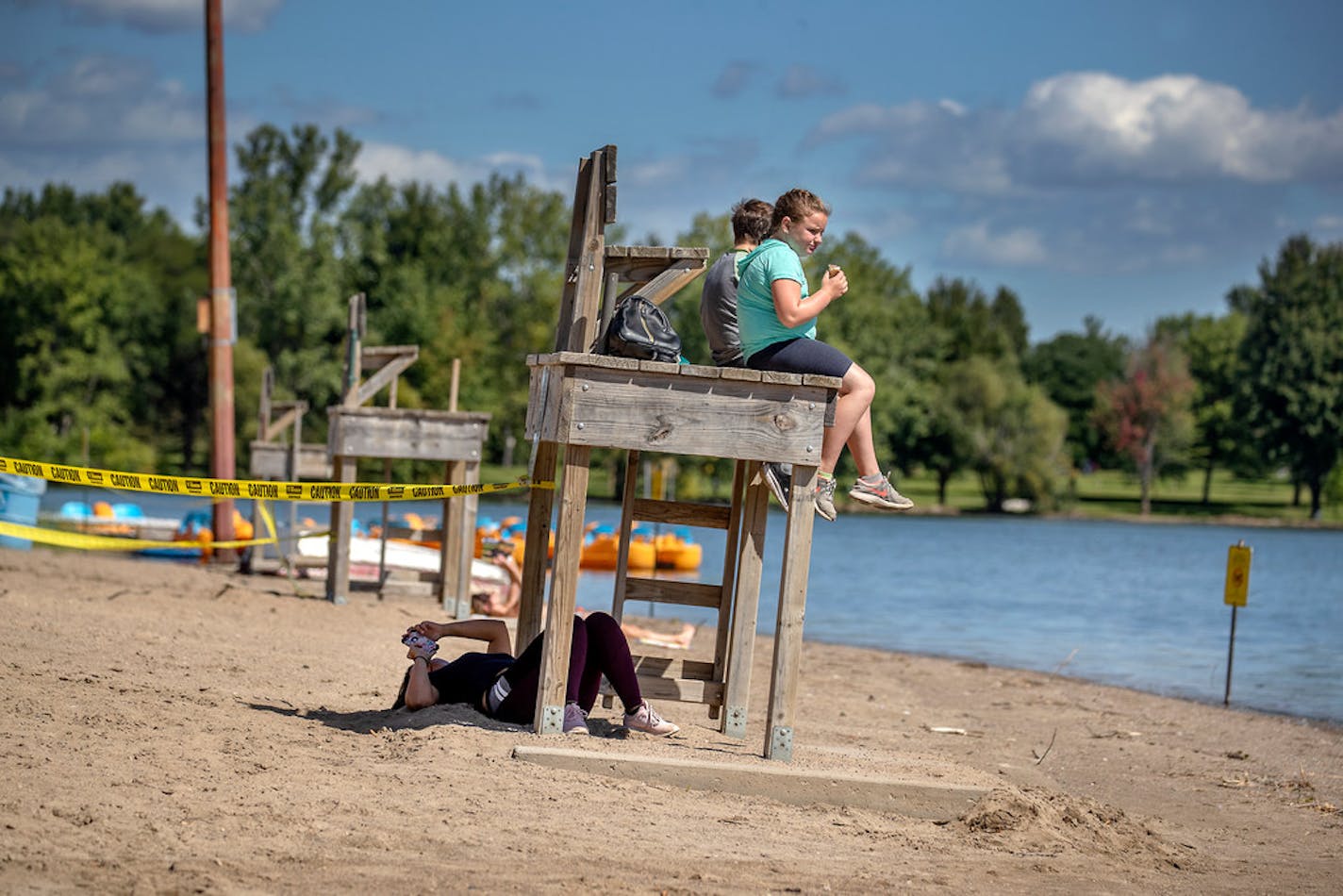 Siblings Karen Lopez, below on phone, JD Rowland, 9, left, and Kiki Rowland, 11, right, took a break for ice cream at Lake Nokomis beach in summer 2019.