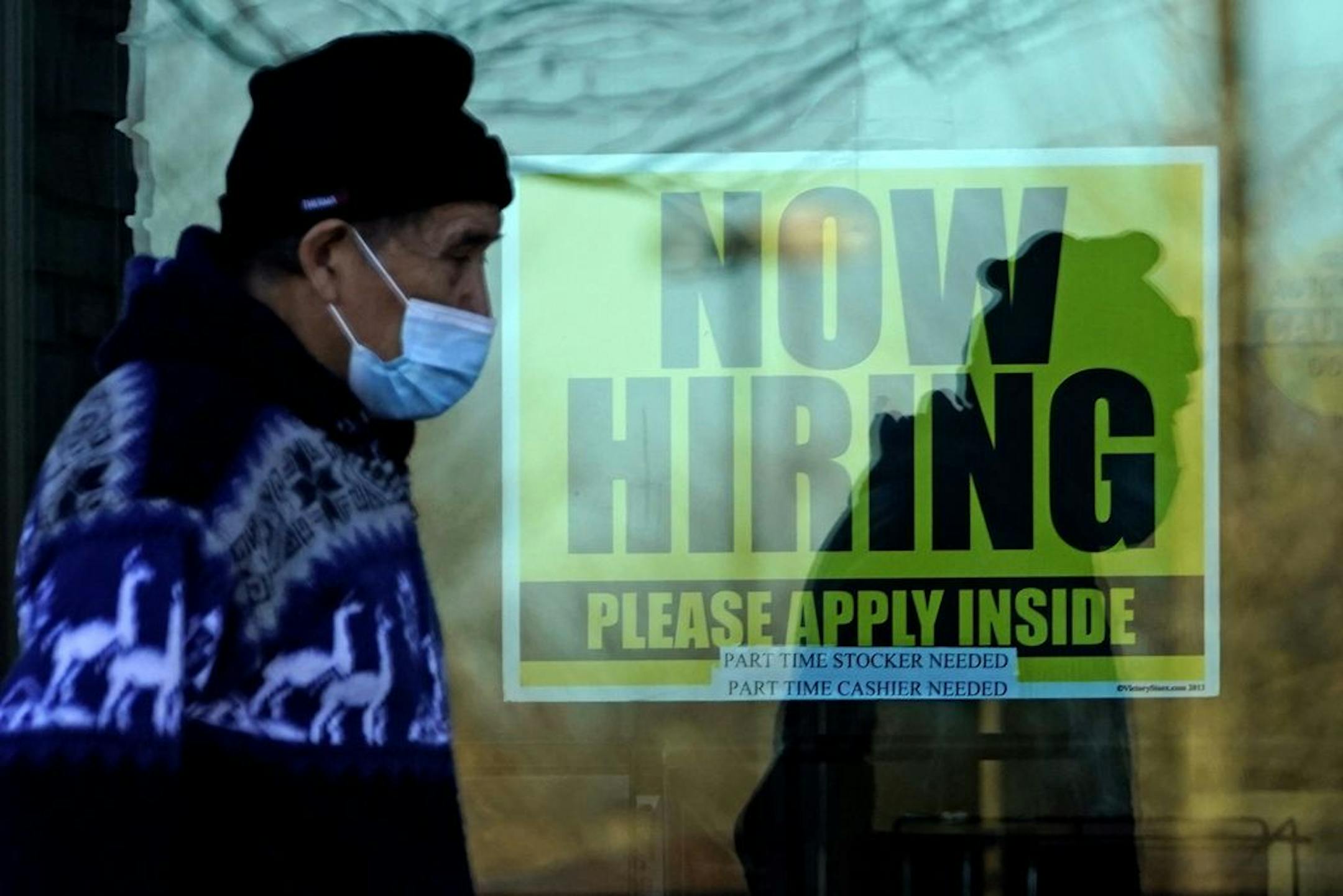 A shopper wears a face mask and he walks past a store displaying a hiring sign in Wheeling, Ill., Saturday, Nov. 28, 2020.